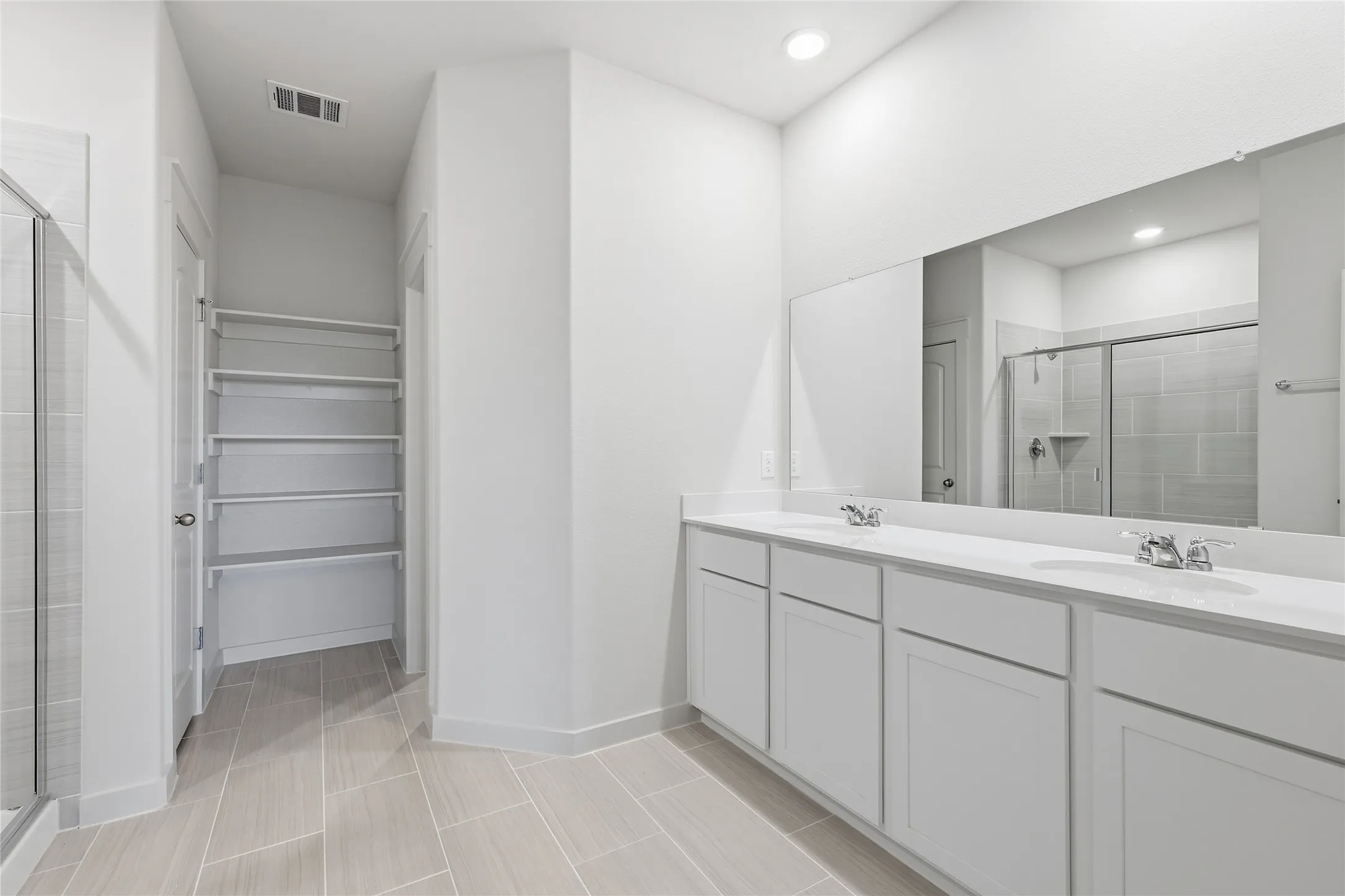 Dual vanity with white cabinetry and integrated sinks, large wall-mounted mirror, and tile flooring