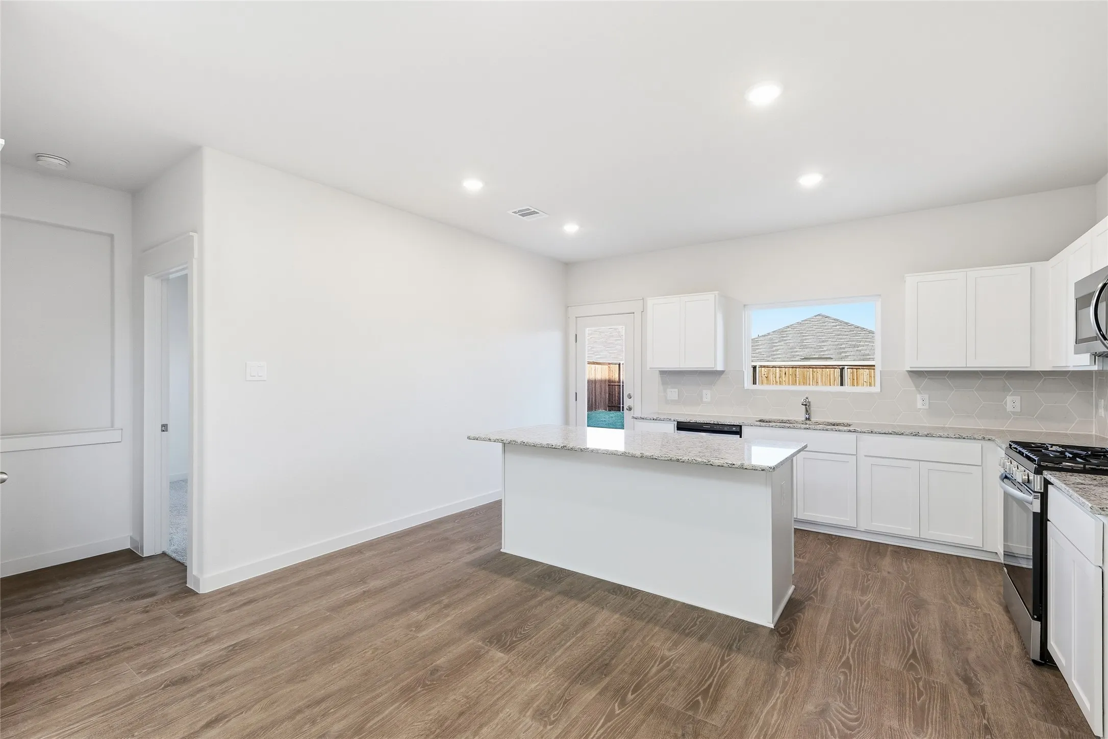 Spacious kitchen featuring an island, white cabinetry, integrated stainless steel appliances, speckled stone countertops, and wood-finish flooring