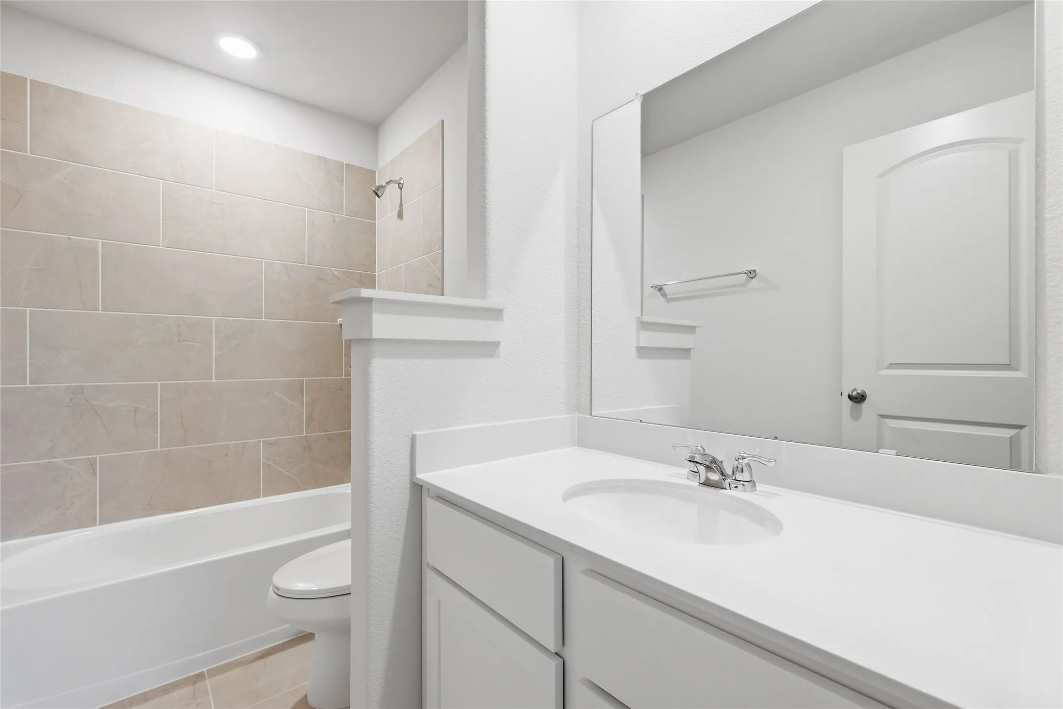 Bathroom featuring a tub/shower combination with large format tile surround, a built-in vanity with an integrated sink, a rectangular mirror, and a contemporary toilet