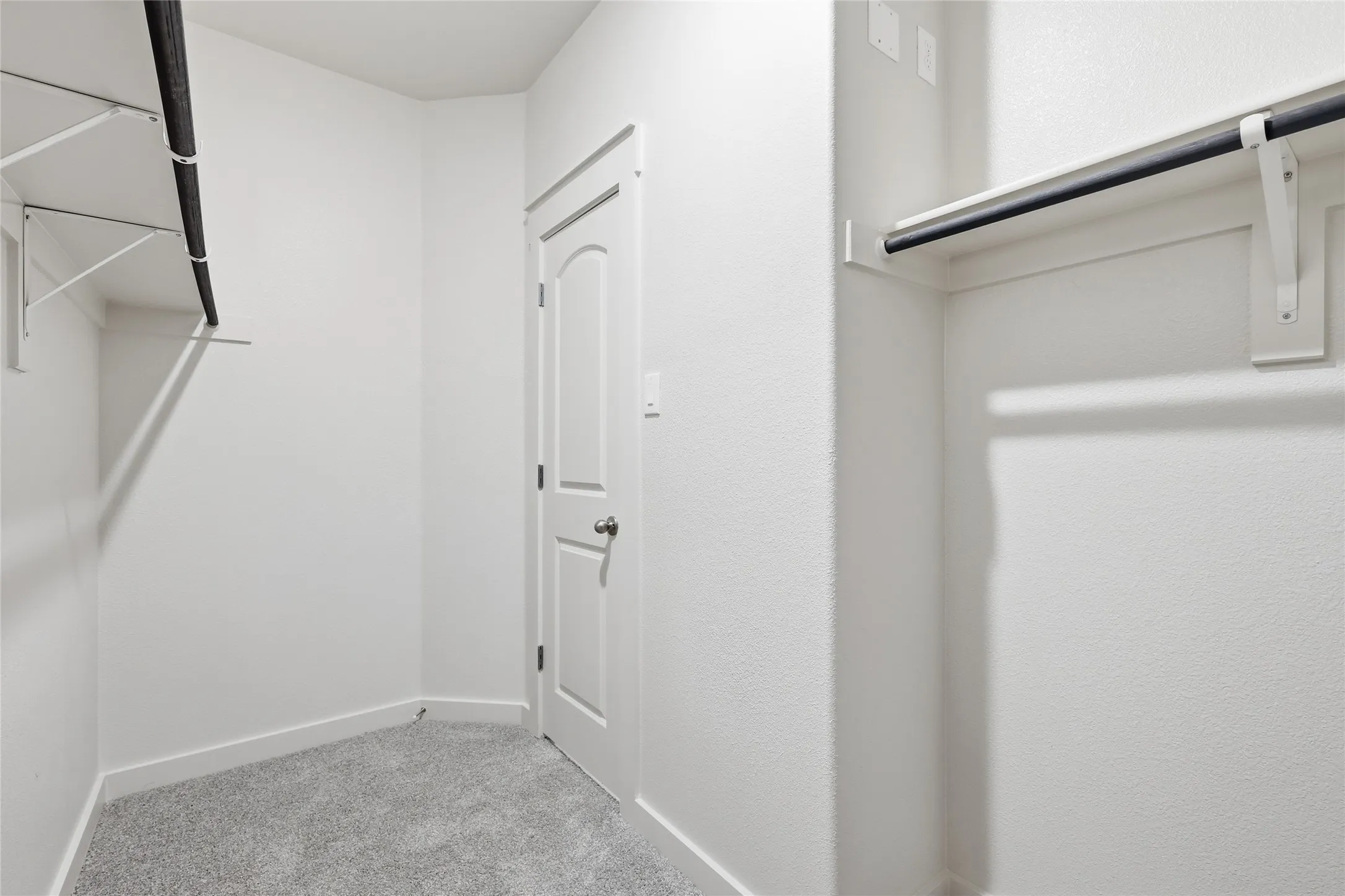 Walk-in closet featuring light grey carpet flooring, white walls, and built-in white shelving with black hanging rods