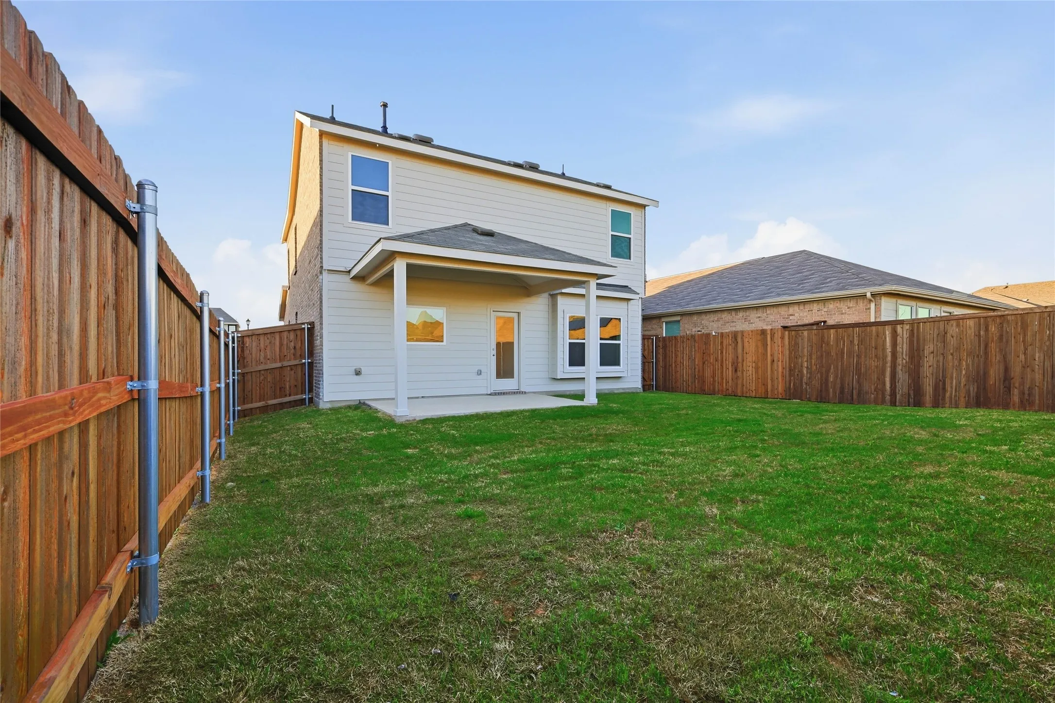 Expansive backyard featuring a manicured lawn, a covered patio, a full privacy fence, and a two-story exterior with light-colored siding