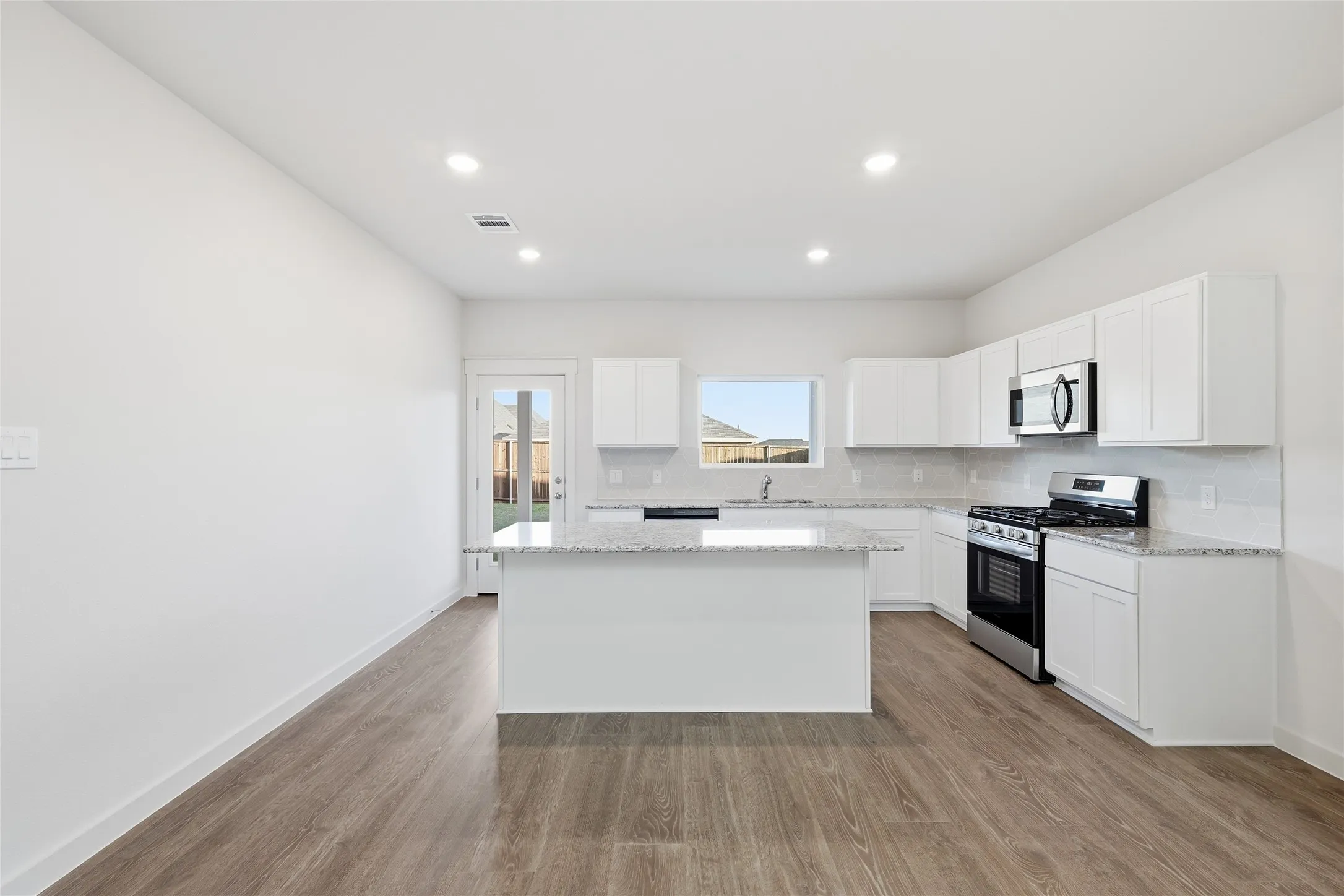 Open-concept kitchen featuring an island, white cabinetry, integrated stainless steel appliances, a tile backsplash, and light-toned countertops