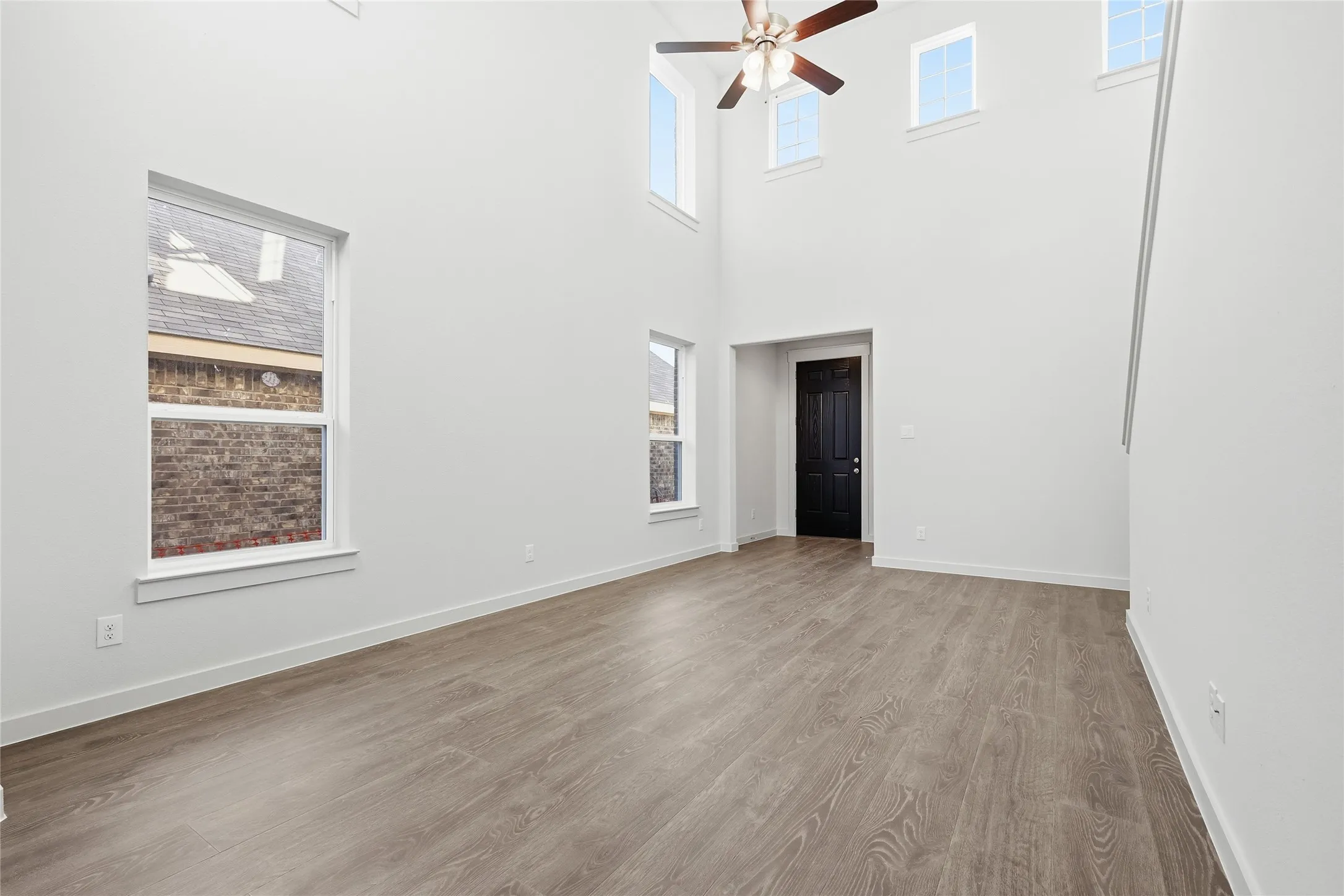 Spacious interior with soaring ceilings, wood-finish flooring, multiple windows, and a ceiling fan