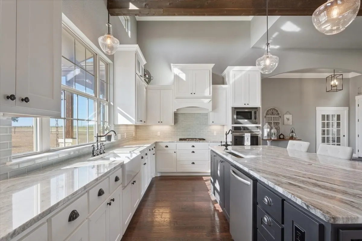 Kitchen with decorative light fixtures, light stone counters, dual tone cabinetry, stainless steel appliances, and backsplash