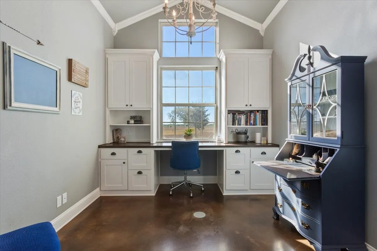 Office area with built in desk, crown molding, concrete floors, hanging lights, and lofted ceiling