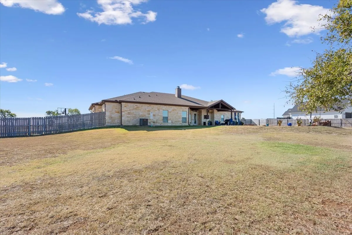 Back of property featuring a fenced backyard, a chimney, stone siding, and a patio