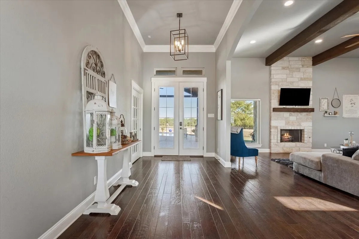 Entryway with french doors, crown molding, dark wood-style flooring, a stone fireplace, and a high ceiling