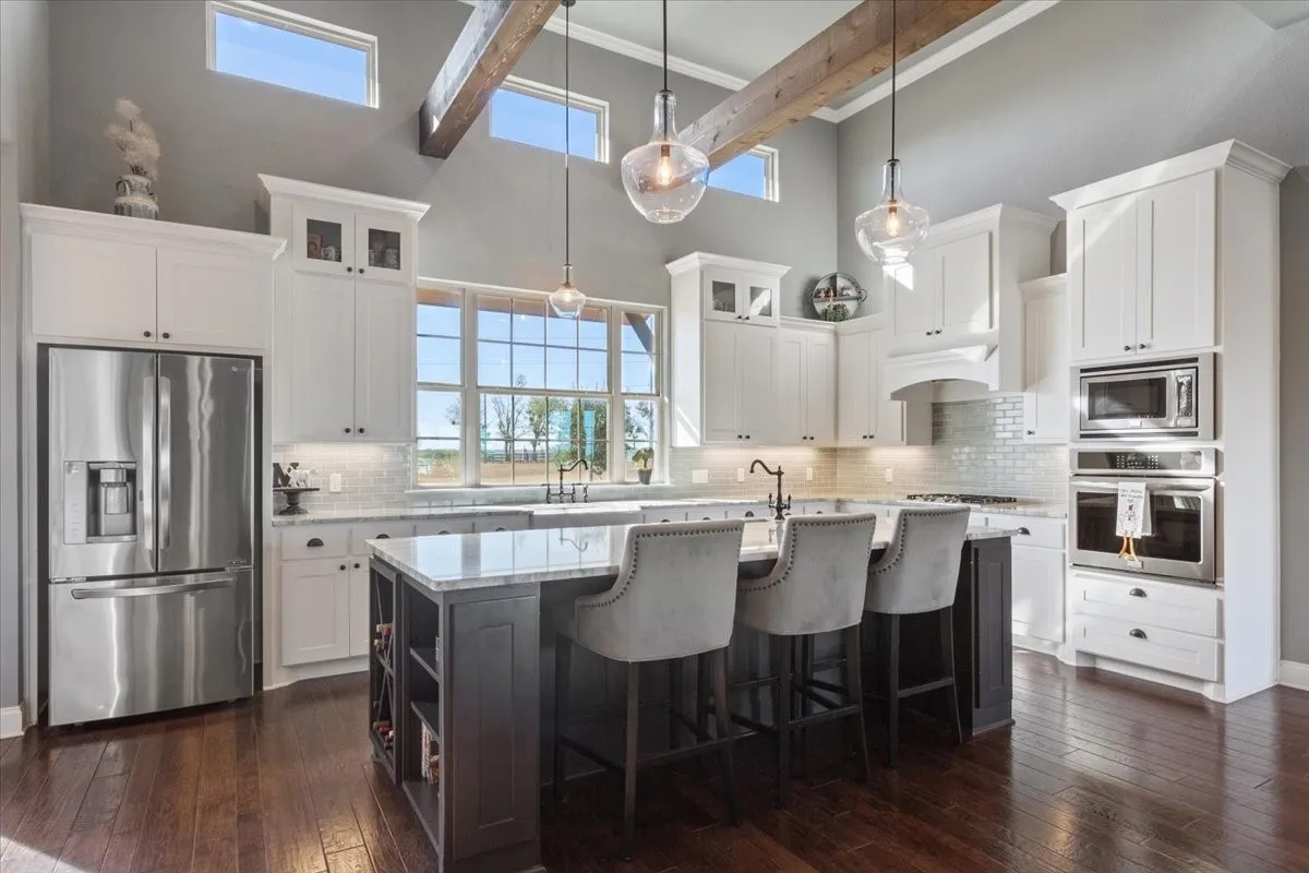 Dual tone kitchen with glass fronted cabinets, stainless steel appliances, an island with sink, a breakfast bar, and two tone cabinetry