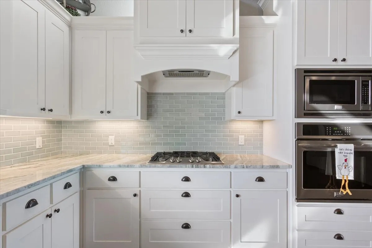 Kitchen featuring white cabinets, stainless steel appliances, light stone counters, and backsplash