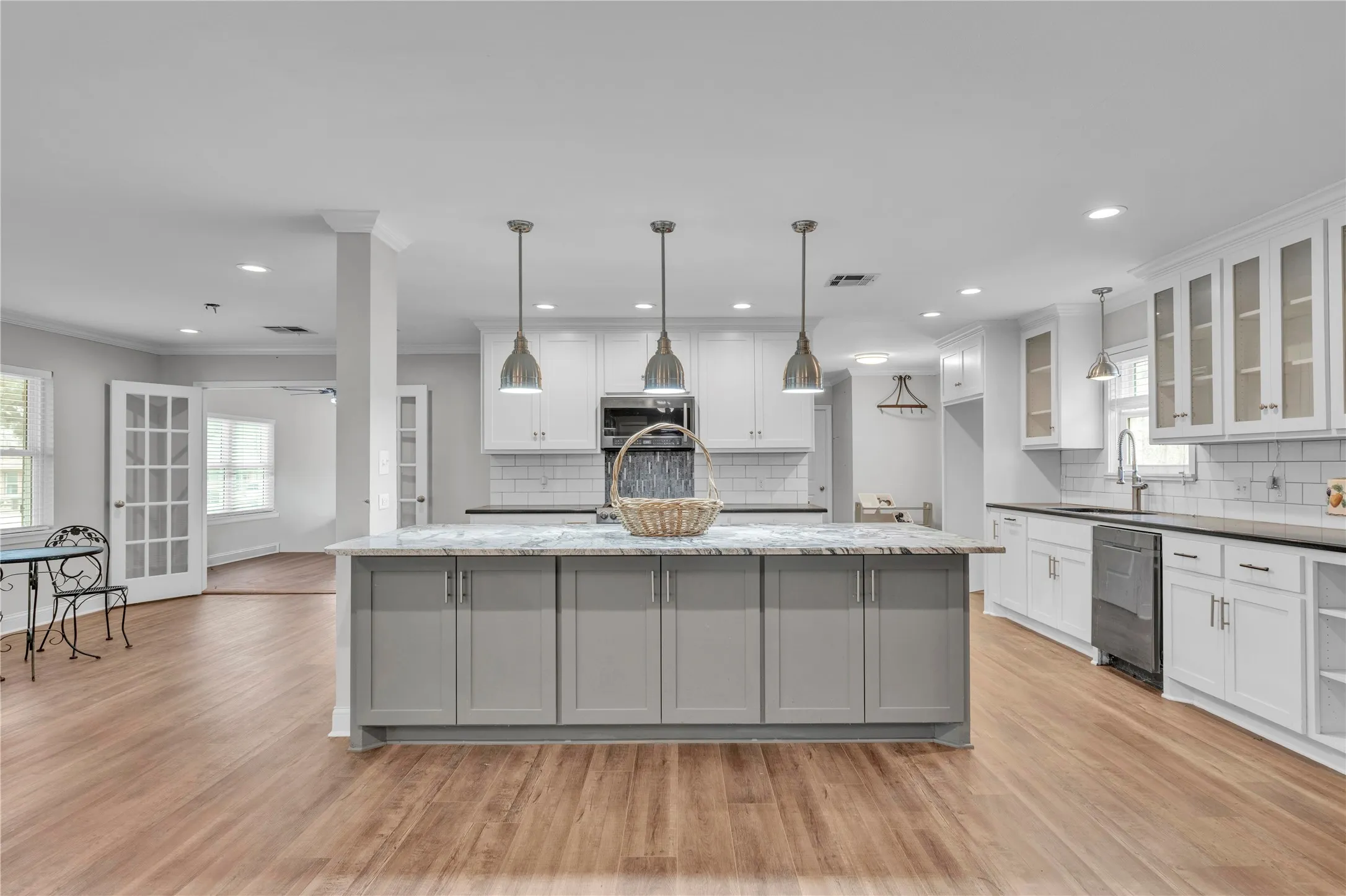 Two tone kitchen featuring a center island with sink, glass fronted cabinets, decorative light fixtures, two tone color scheme, and light wood-type flooring