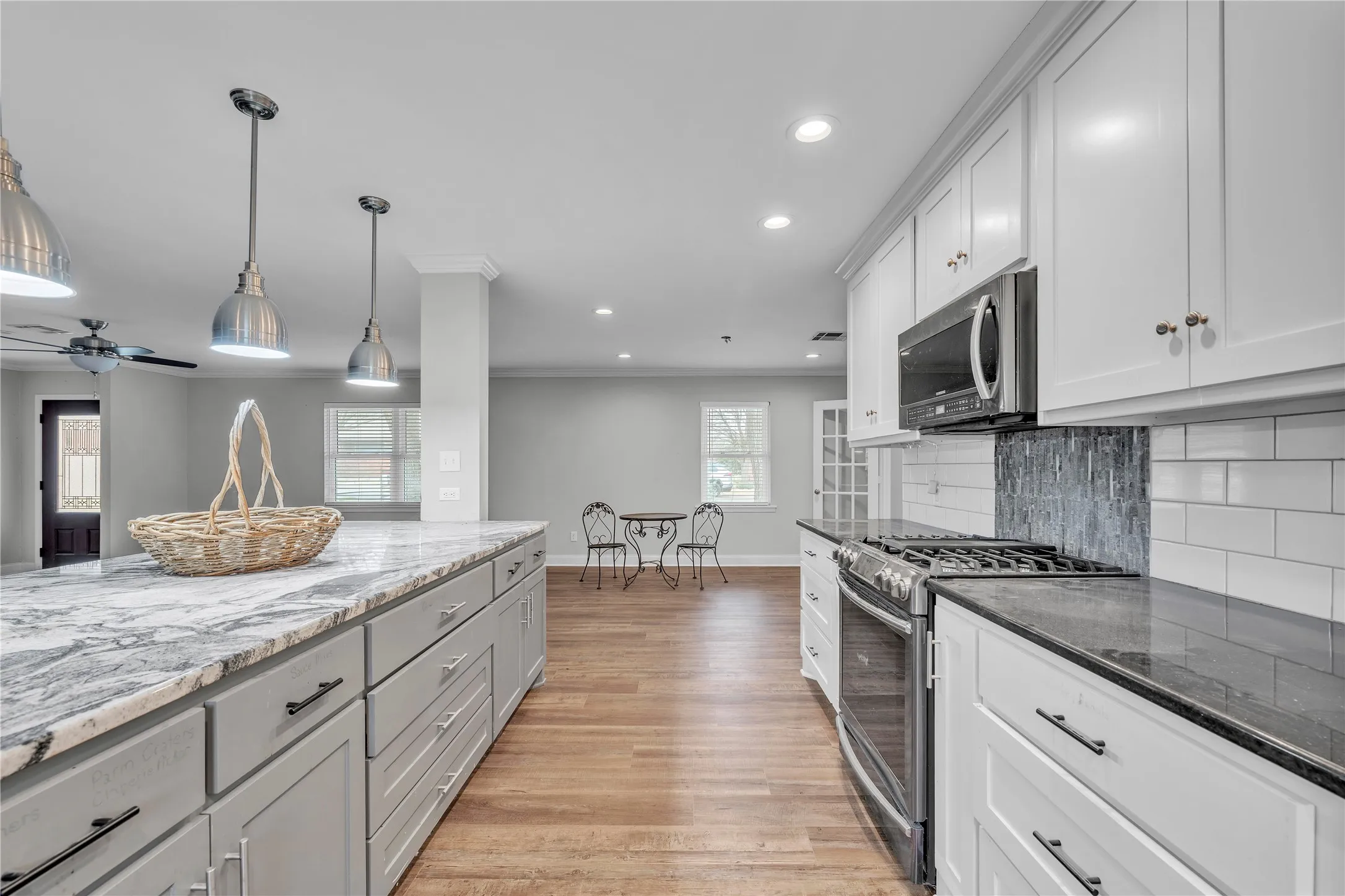Dual tone kitchen featuring stainless steel appliances, hanging light fixtures, dark stone counters, two tone cabinets, and light wood-style flooring