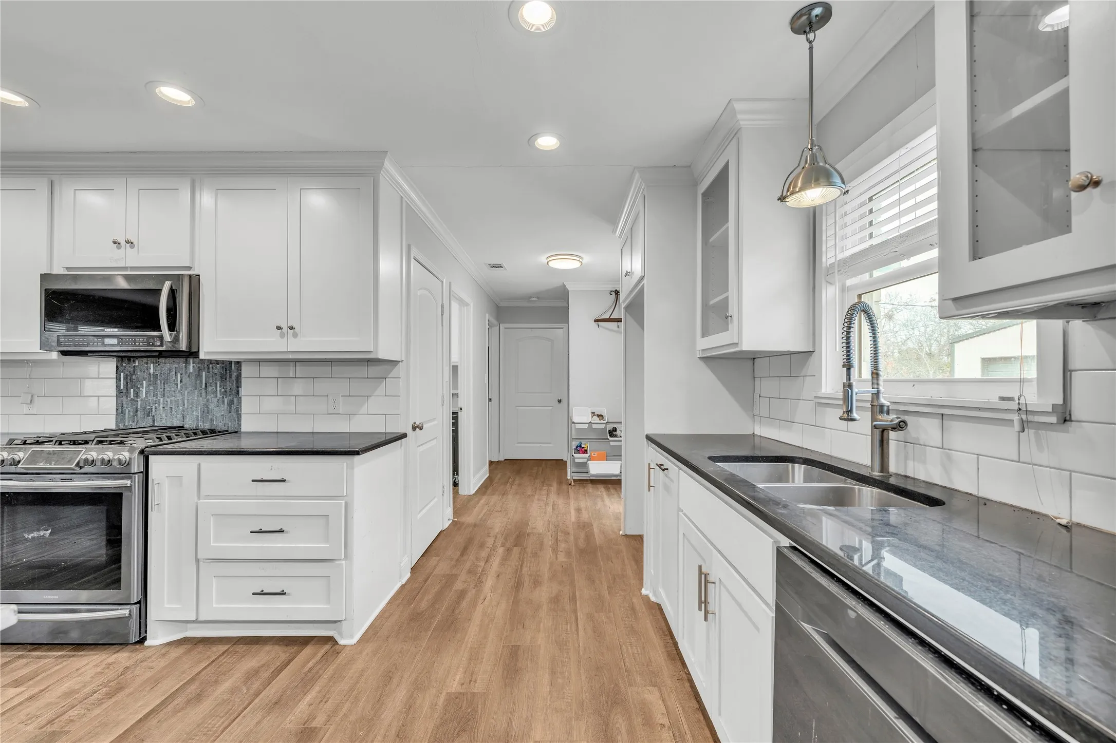 Kitchen featuring decorative light fixtures, white cabinets, stainless steel appliances, and crown molding