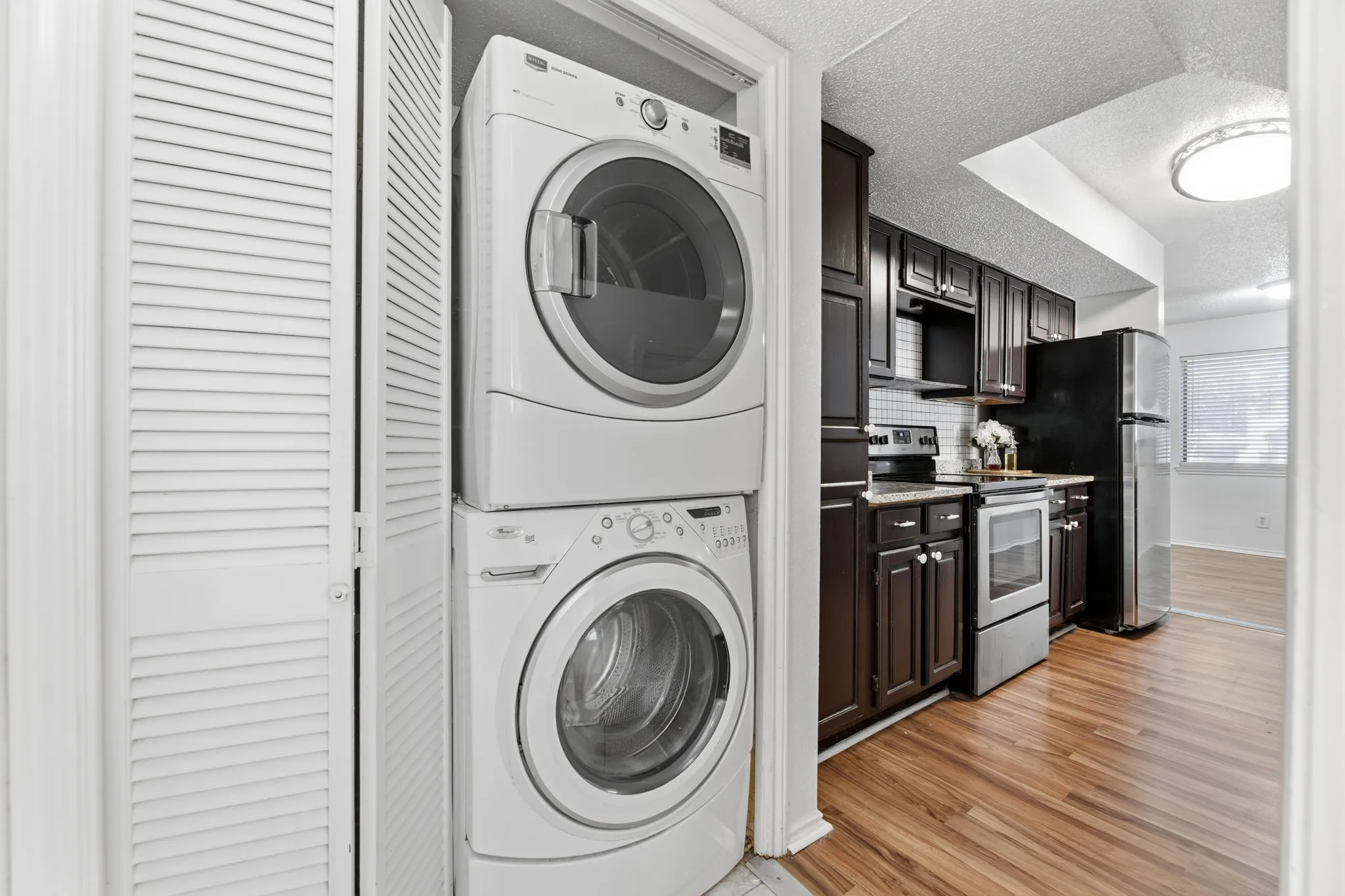 Laundry area with stacked washing machine and dryer, light wood-type flooring, and a textured ceiling
