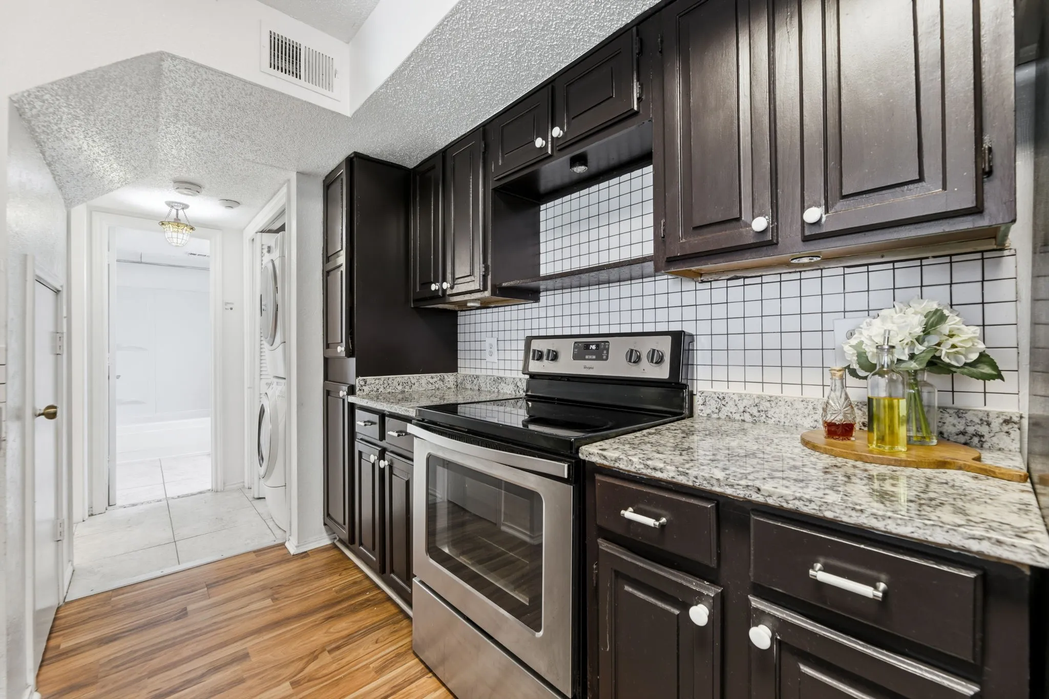 Kitchen with electric stove, light wood finished floors, a textured ceiling, light stone counters, and stacked washer and dryer