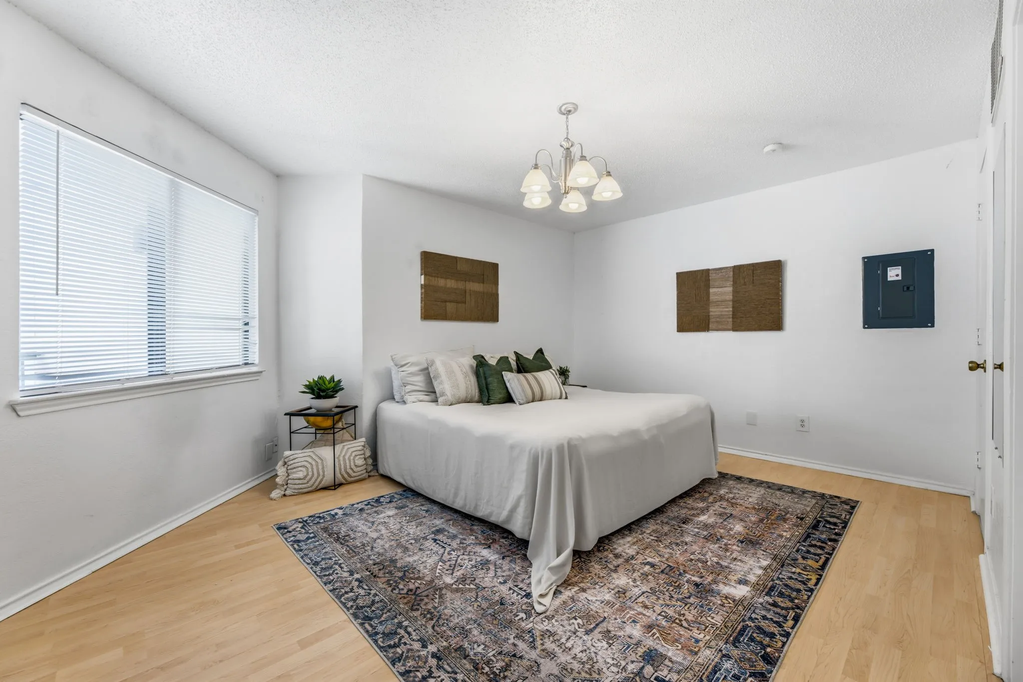 Bedroom featuring light wood finished floors, electric panel, hanging lights, and a textured ceiling