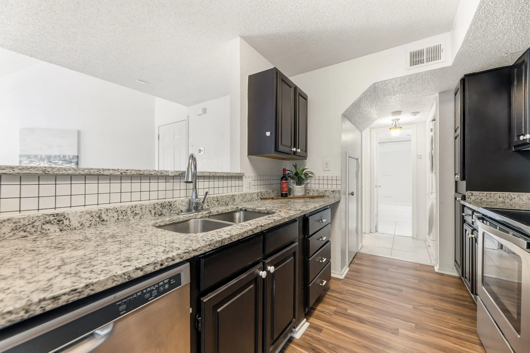 Kitchen with a textured ceiling, stainless steel appliances, light stone countertops, and dark wood-type flooring