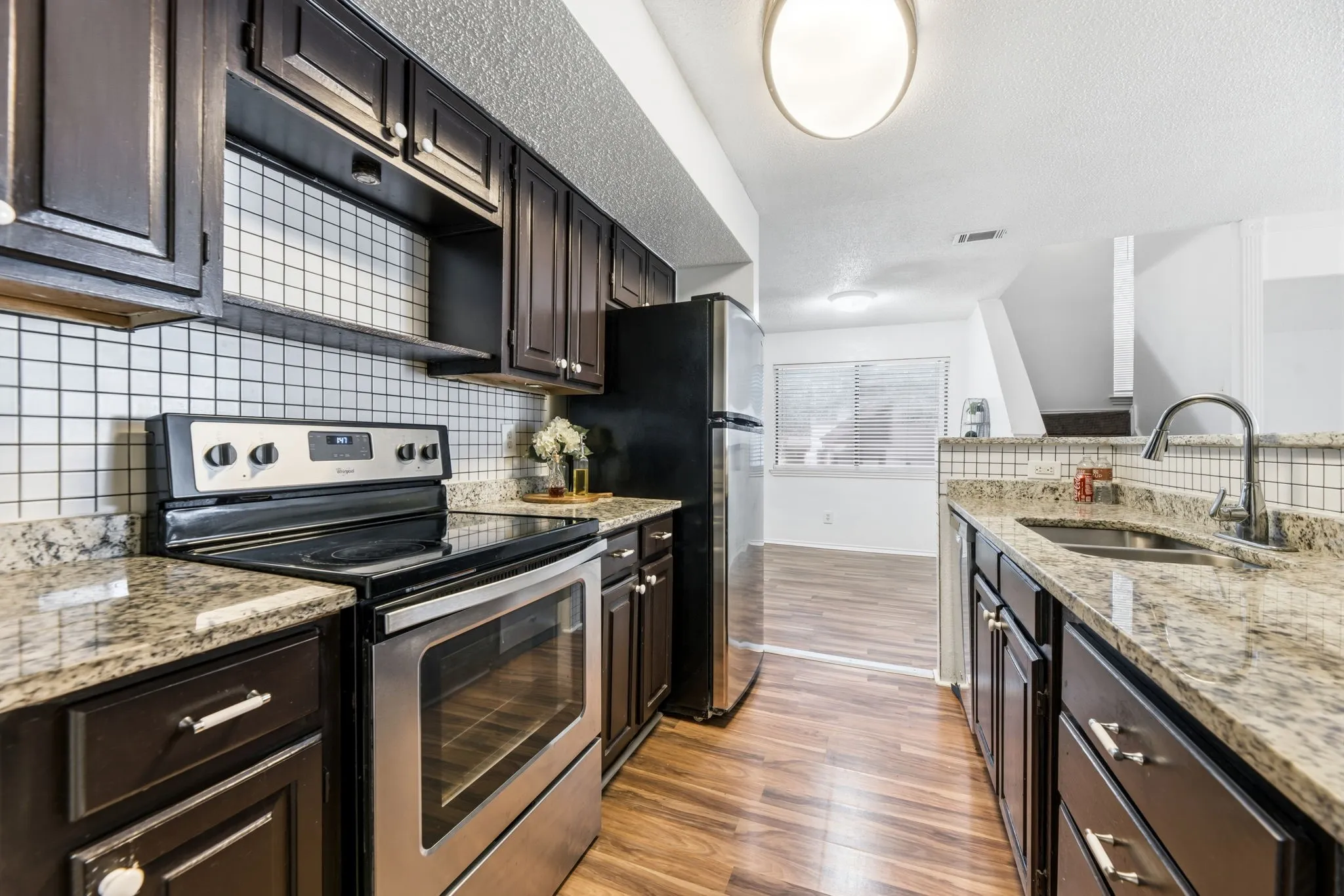 Kitchen with stainless steel appliances, light stone counters, light wood-style floors, dark wood finish cabinetry, and tasteful backsplash