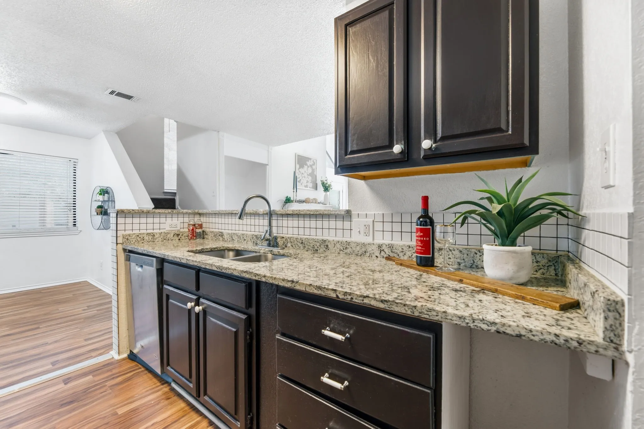 Kitchen featuring backsplash, light stone countertops, light wood finished floors, dishwasher, and a textured ceiling