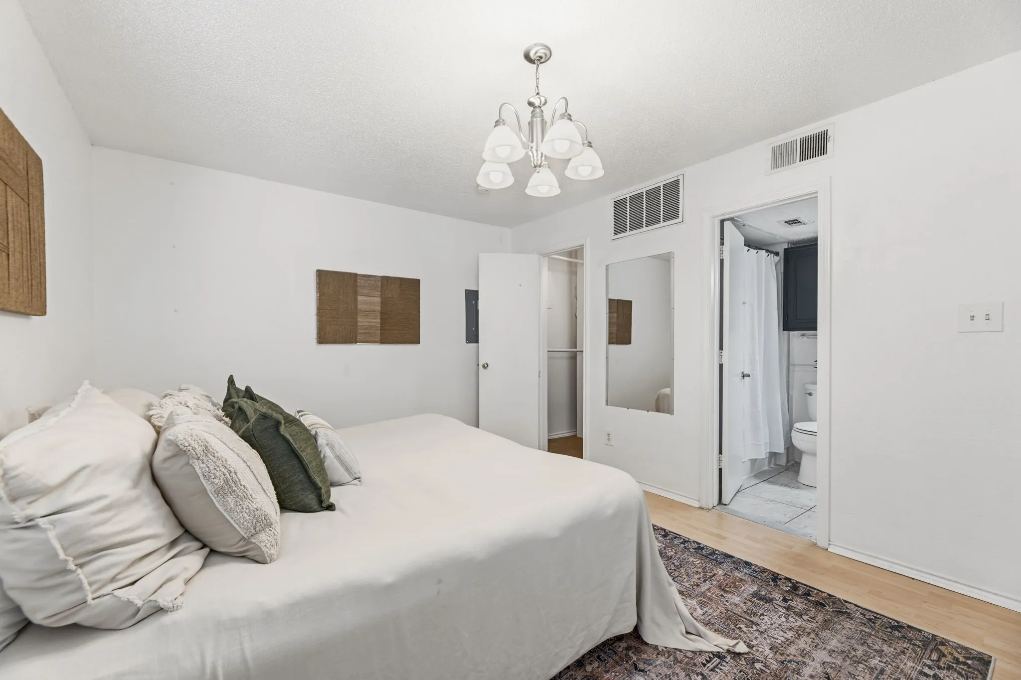 Bedroom featuring light wood-style floors, a chandelier, ensuite bath, and a textured ceiling