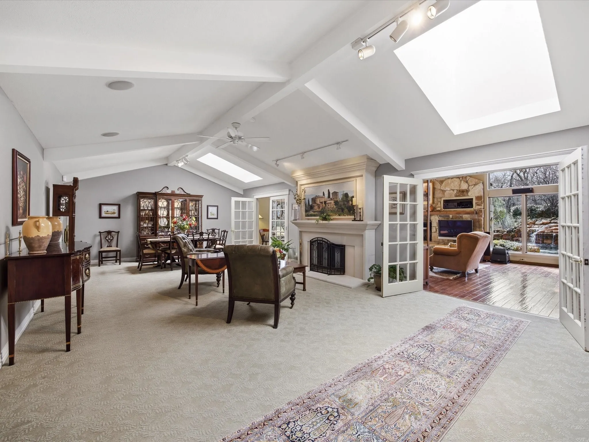 Living room with a skylight, a fireplace with raised hearth, light carpet, beamed ceiling, and rail lighting