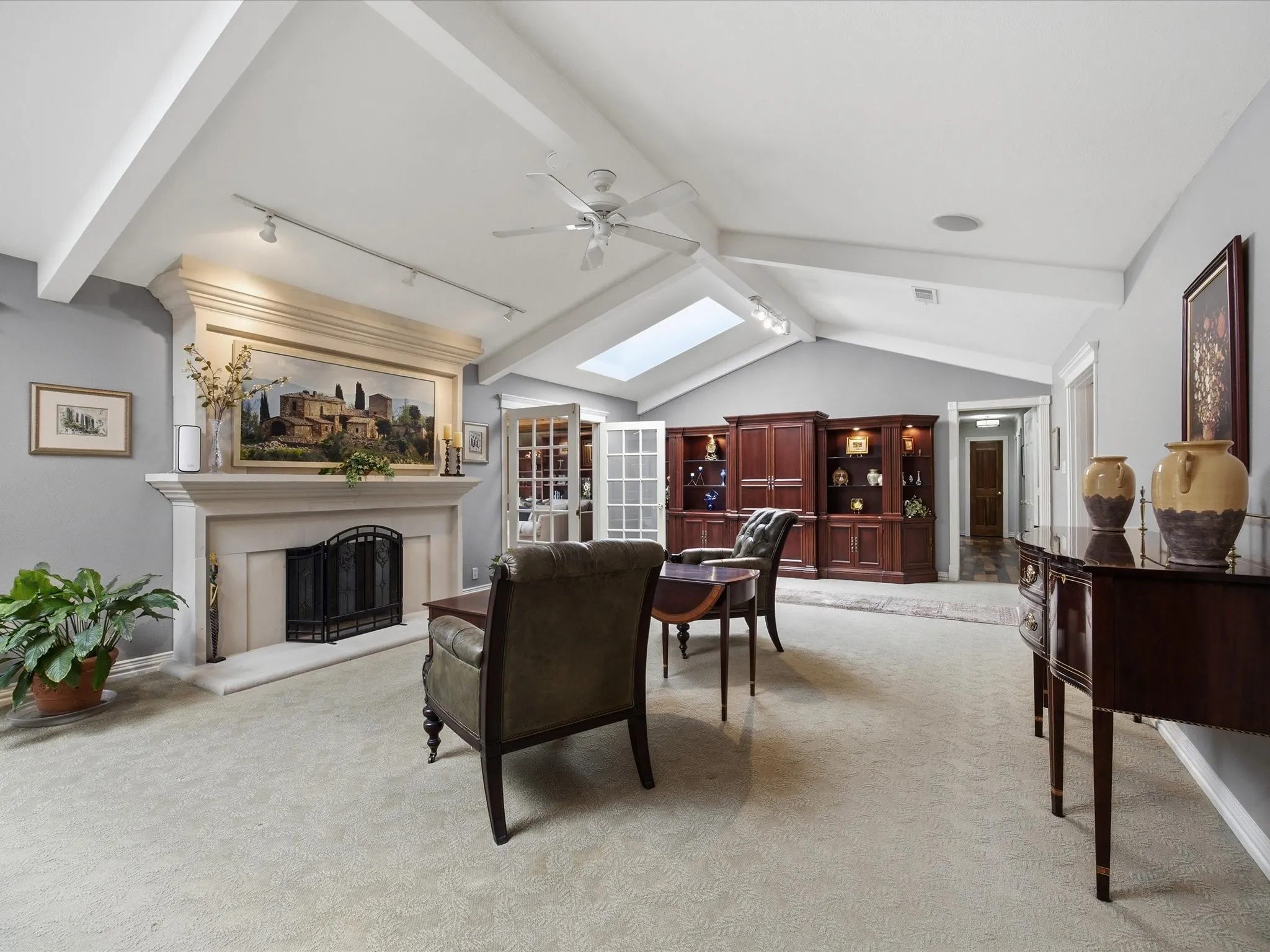 Living room with beamed ceiling, light colored carpet, a fireplace with raised hearth, ceiling fan, and a skylight