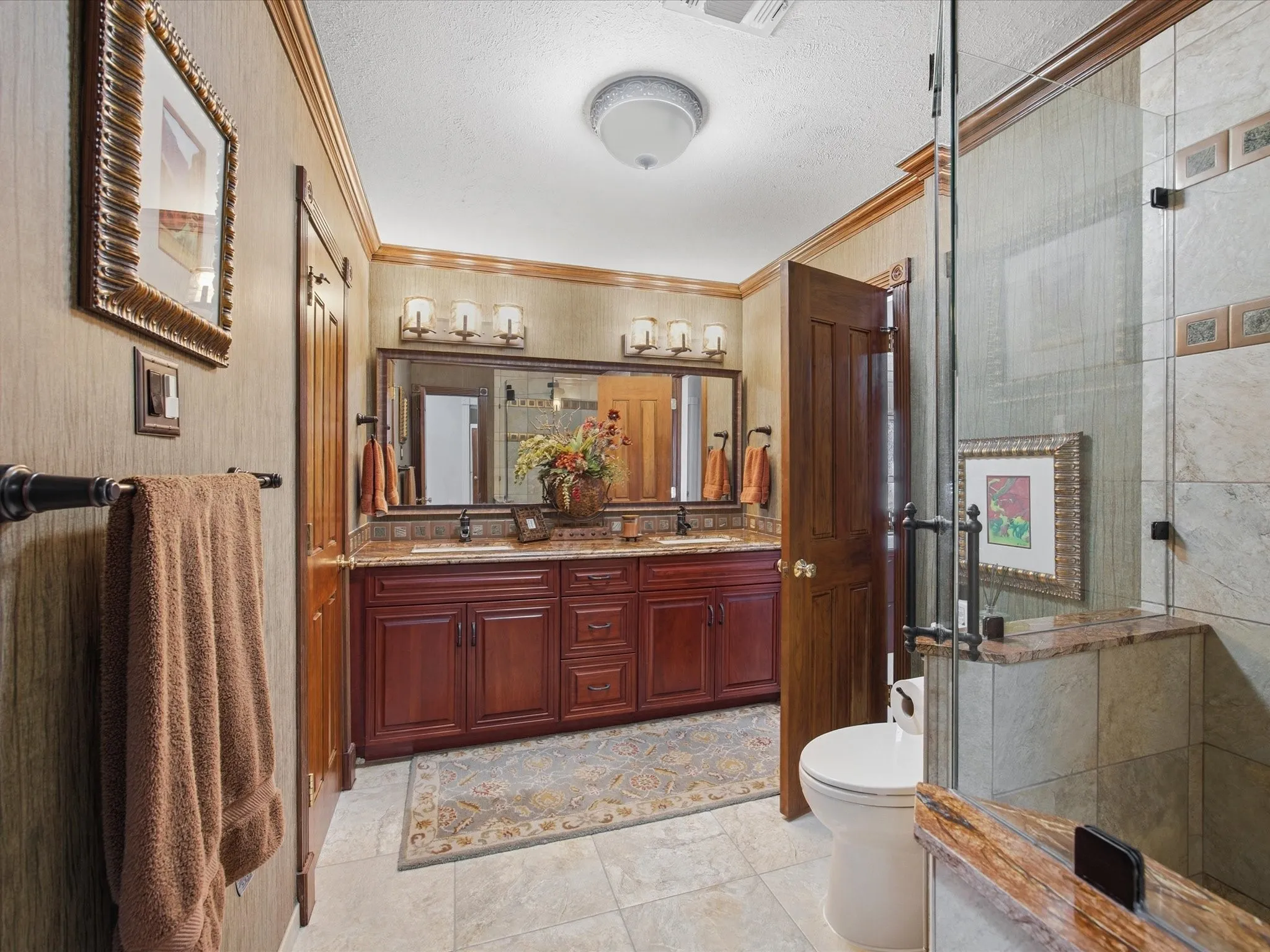 Full bathroom with double vanity, a textured ceiling, a shower stall, crown molding, and light tile patterned flooring