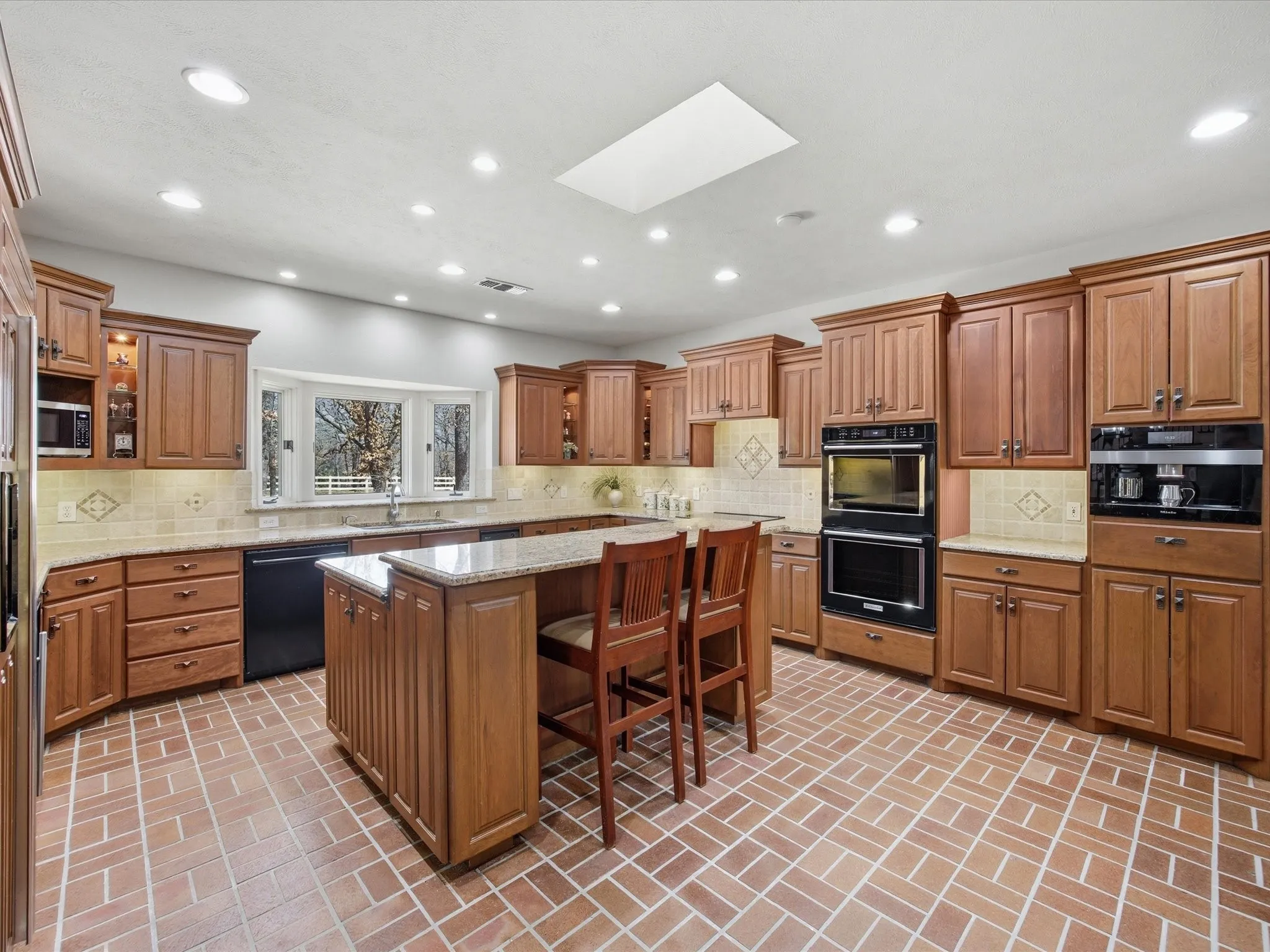 Kitchen featuring a kitchen breakfast bar, wood finish cabinets, a skylight, black appliances, and a kitchen island
