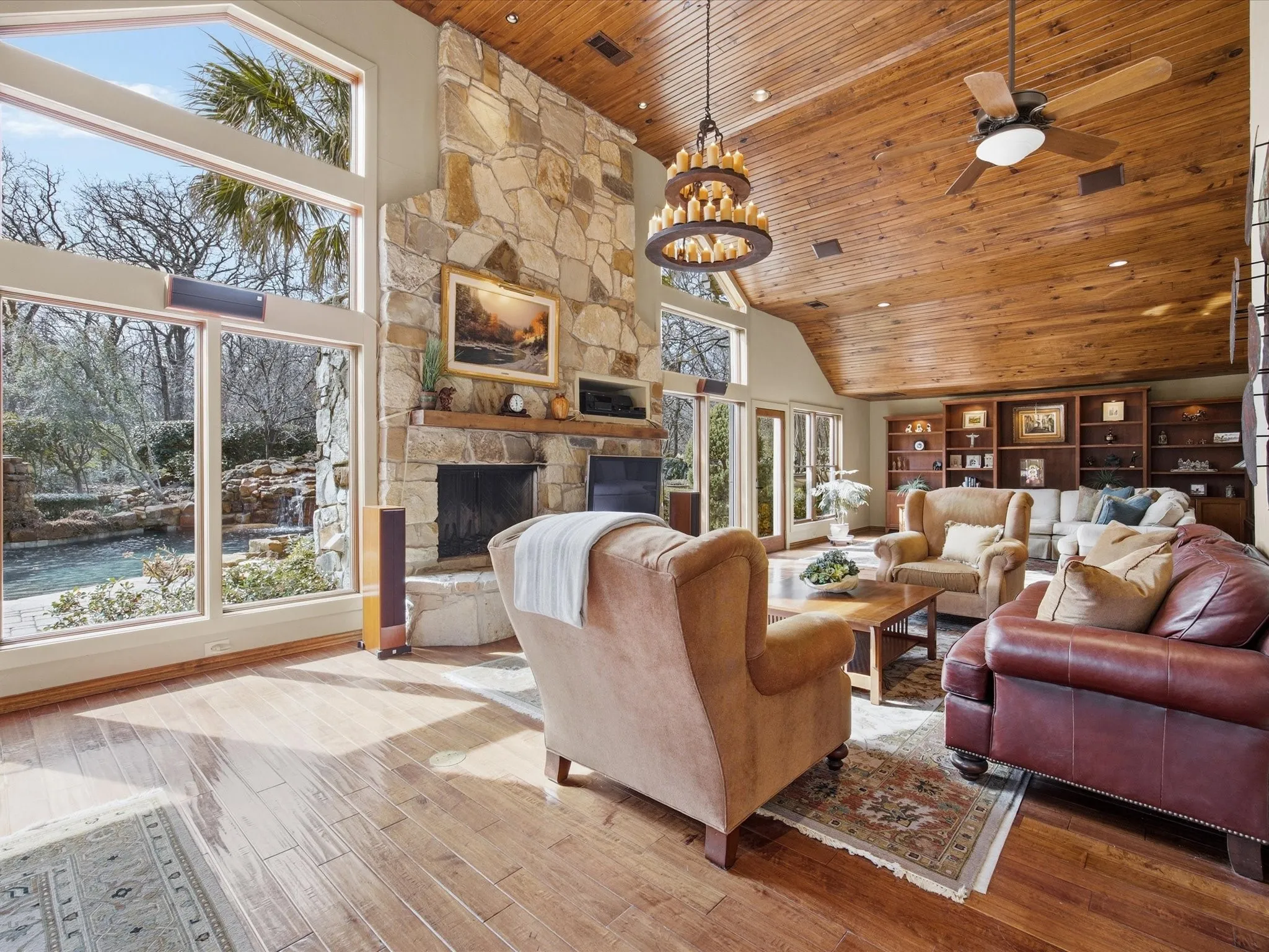 Living room featuring a vaulted wood ceiling, wood finished floors, a stone fireplace, ceiling fan, and suspended lighting