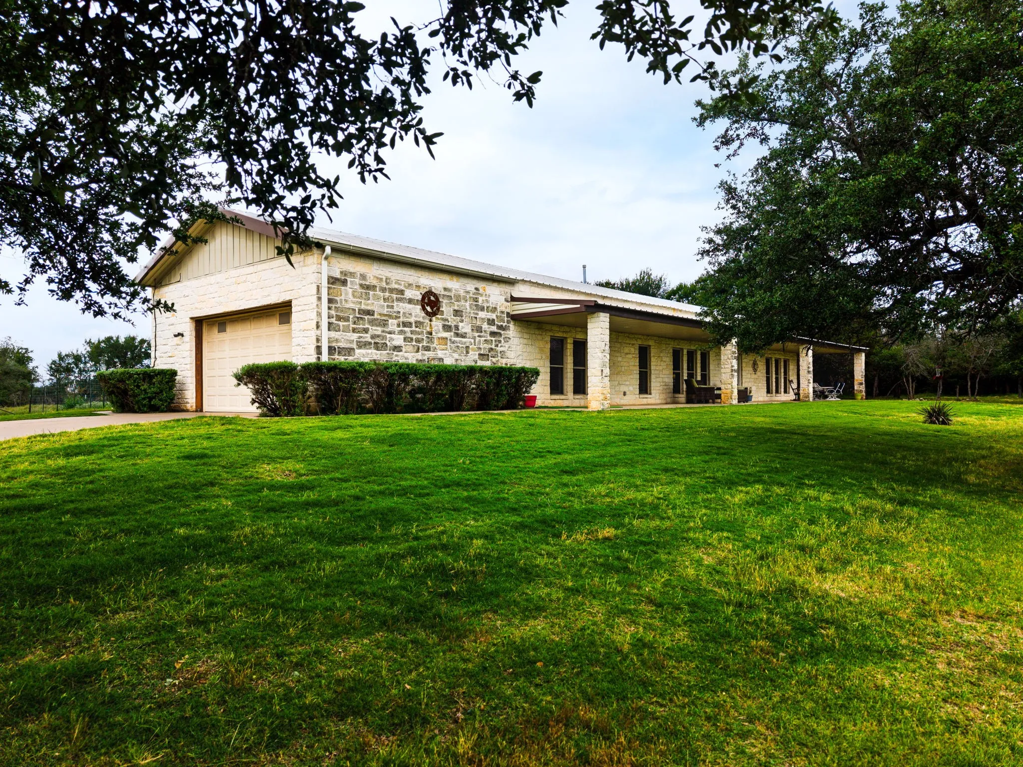 Spacious property featuring a stone and siding exterior, an attached garage, a covered front porch, and mature trees