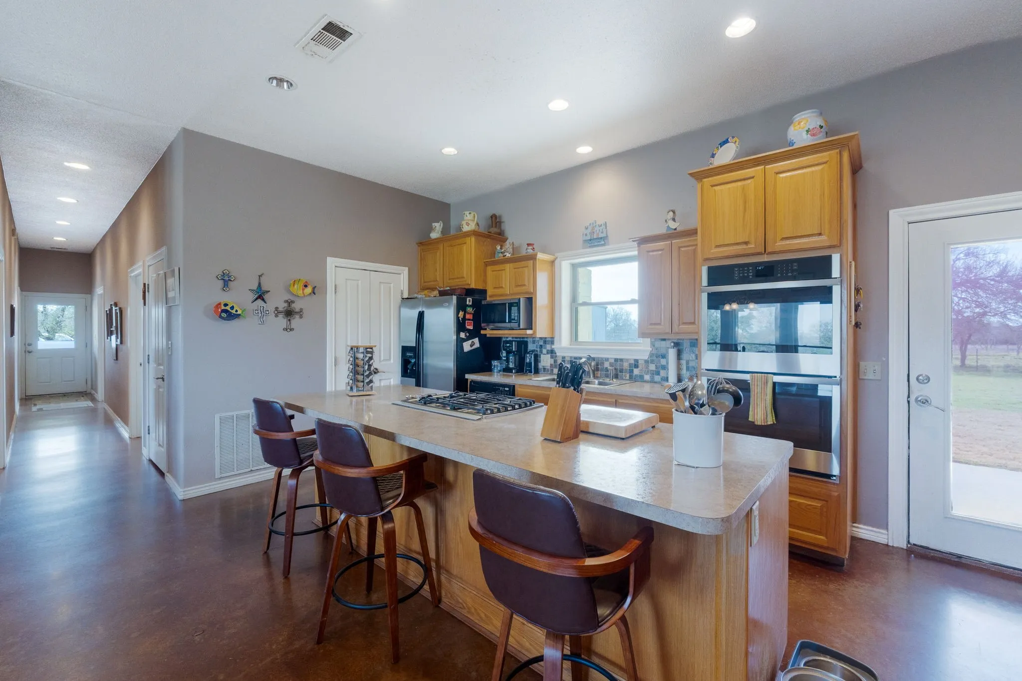 Kitchen with finished concrete flooring, stainless steel appliances, a kitchen breakfast bar, a center island, and decorative backsplash
