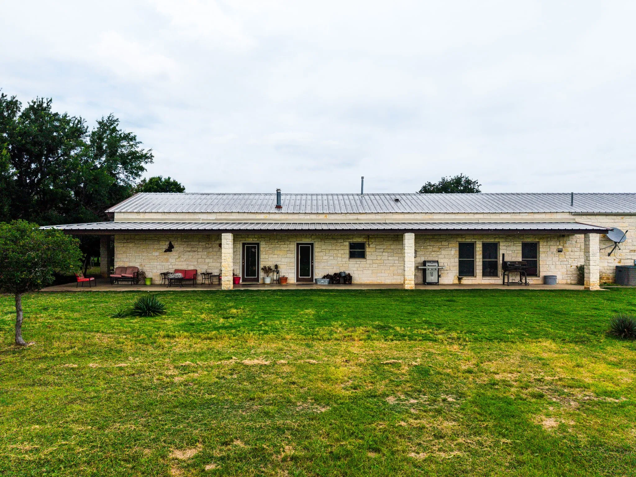 Stone exterior residence featuring a corrugated metal roof and a full-length covered patio