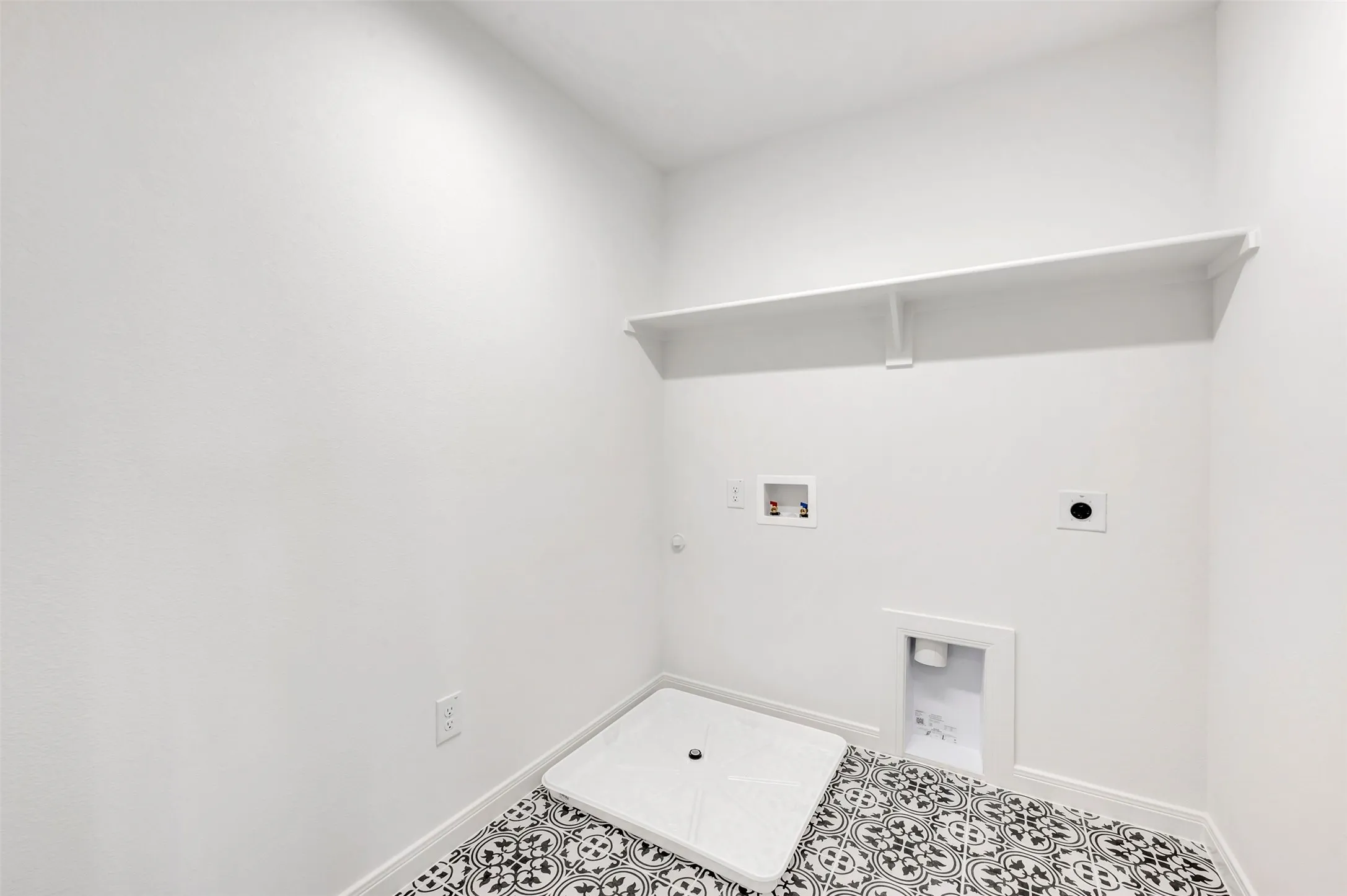 Utility space featuring patterned black and white floor tiles, a built-in white shelf, and all-white walls