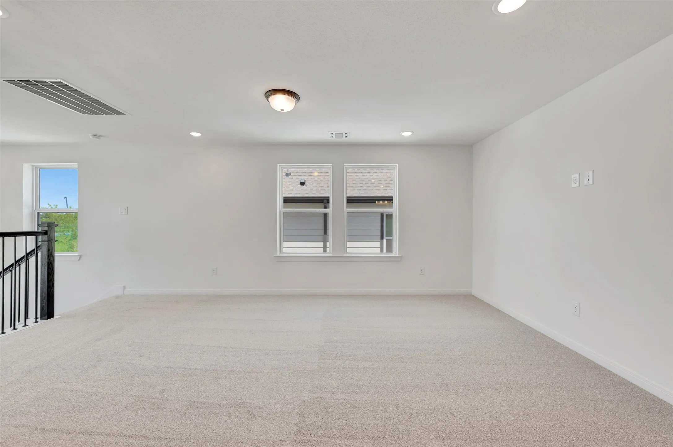 Spacious room featuring light-colored carpeting, white painted walls, and multiple windows