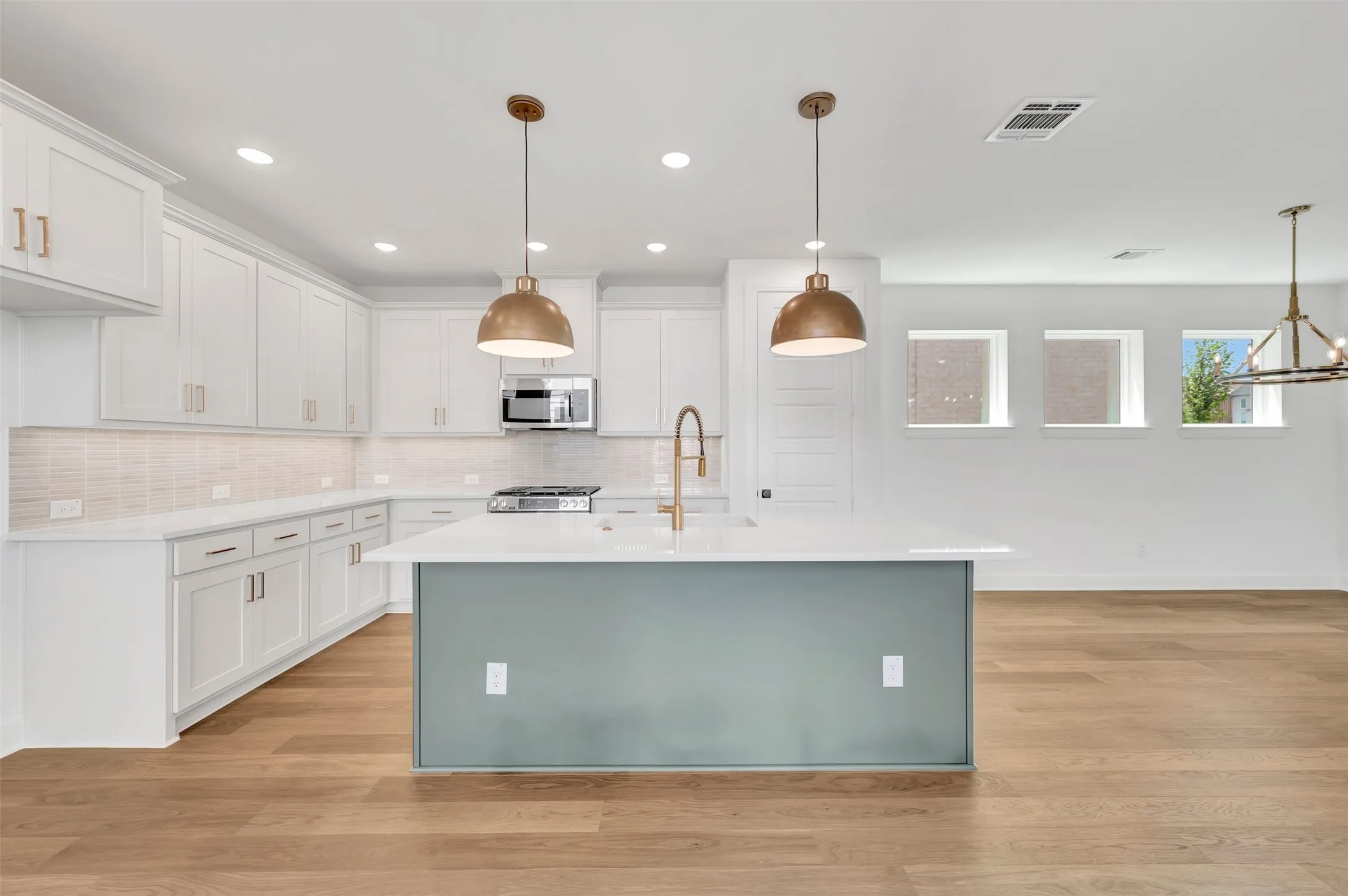 Contemporary kitchen featuring white shaker cabinetry, light-toned wood-finish flooring, a central island with a contrasting base and solid surface countertop, stainless steel appliances, and two brass pendant lights