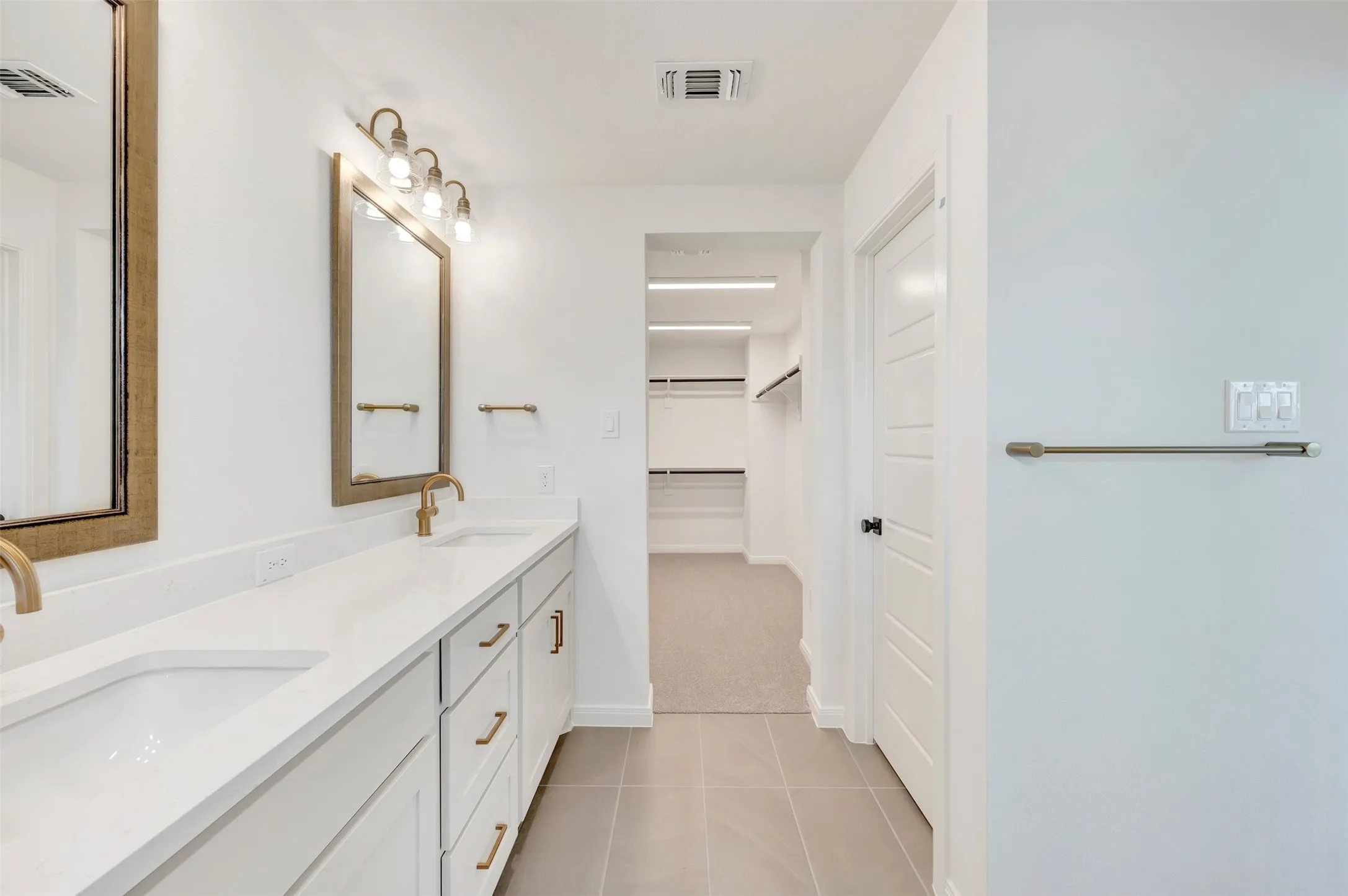 Dual vanity with integrated sinks, white cabinetry, brass hardware, and rectangular mirrors with brass-finish frames