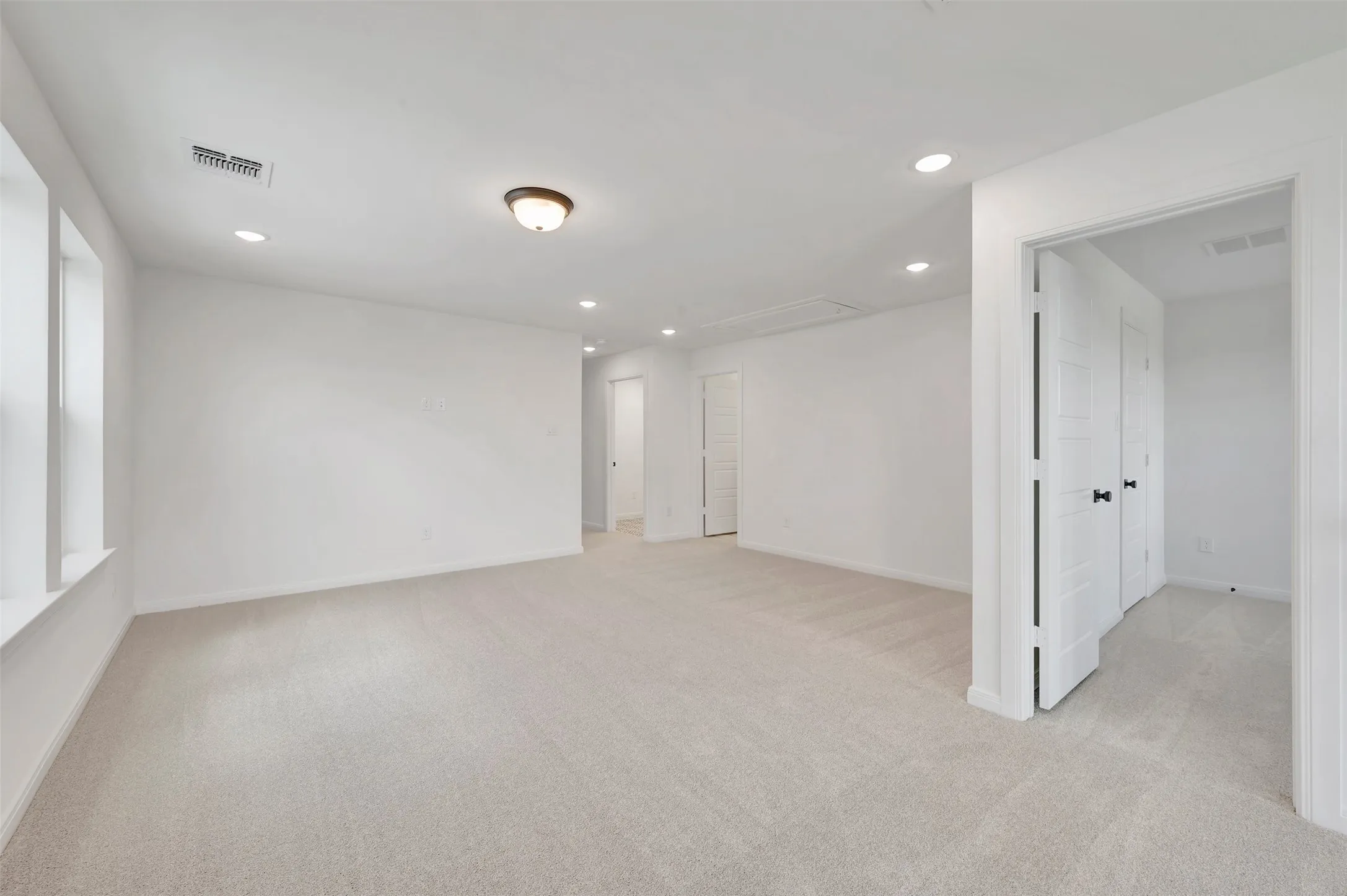 Spacious room featuring light-toned carpeting, multiple recessed lights, and white paneled doors with dark hardware