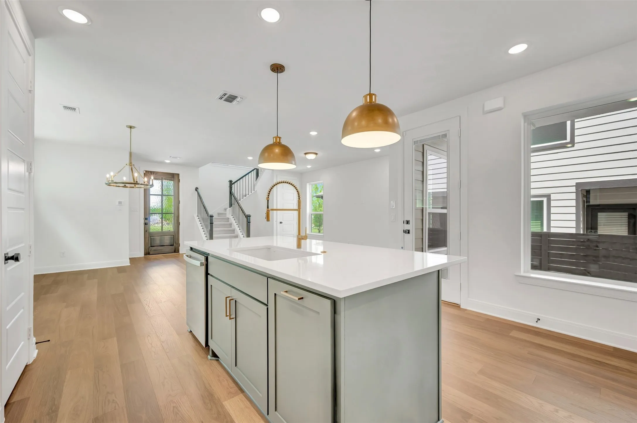 Kitchen island with a light grey cabinet finish, white countertop, and gold-toned pendant lighting
