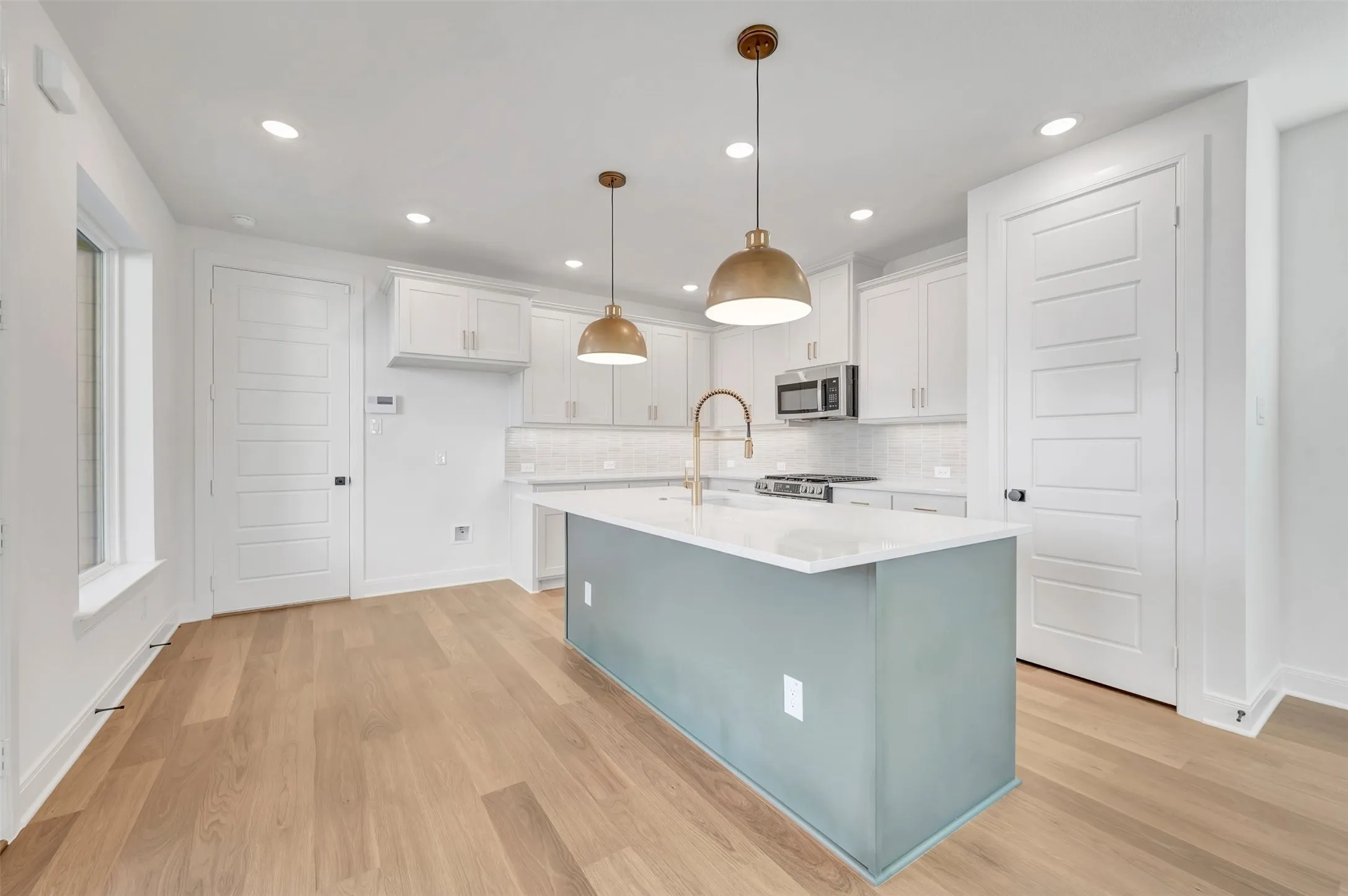 Open-concept kitchen featuring a central island with a light blue-grey finish, white countertops, stainless steel appliances, white cabinetry, and wood-finish flooring