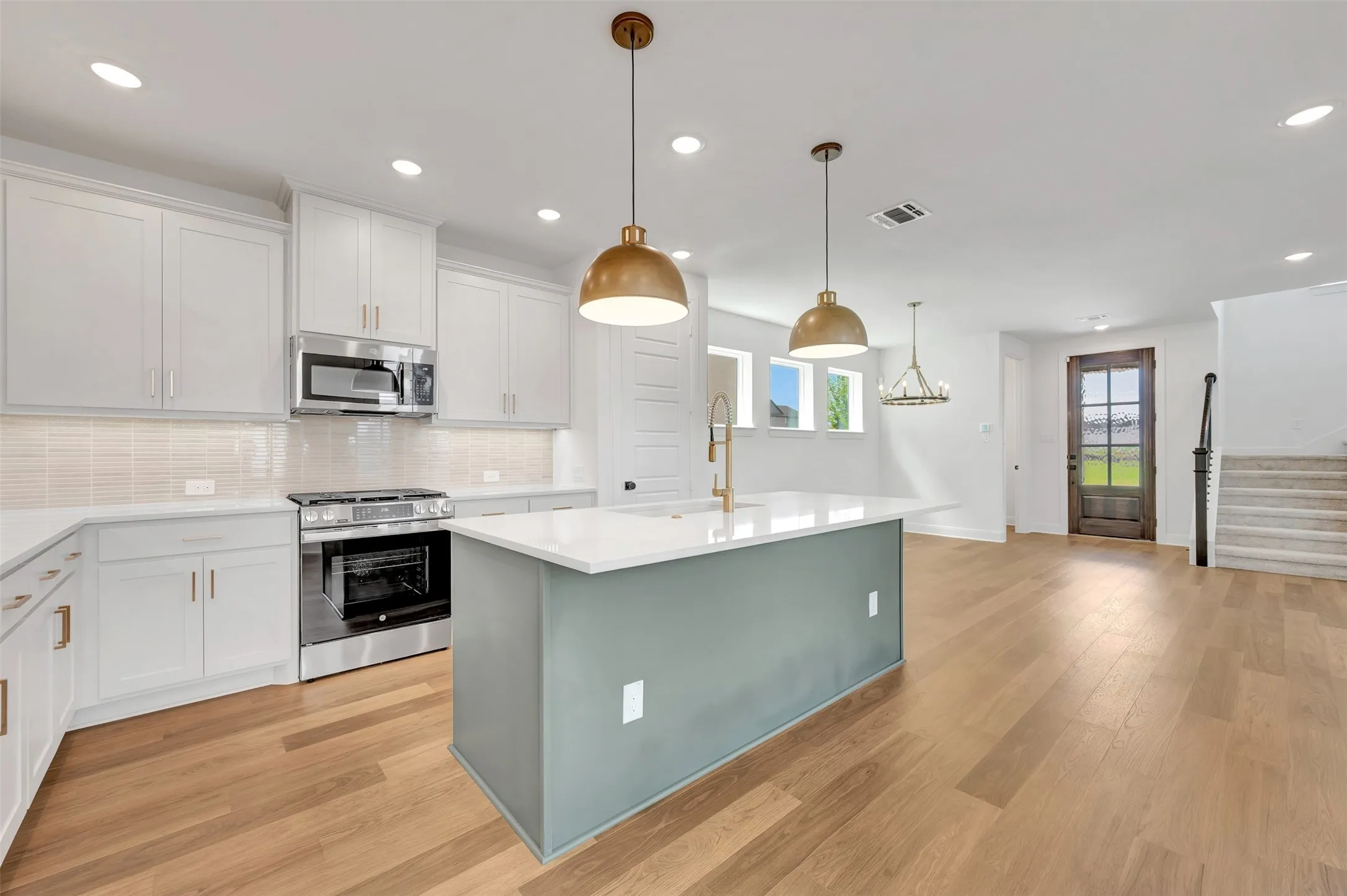 Modern kitchen featuring a central island with a light teal base, white countertops, stainless steel appliances, white cabinetry, and wood-finish flooring