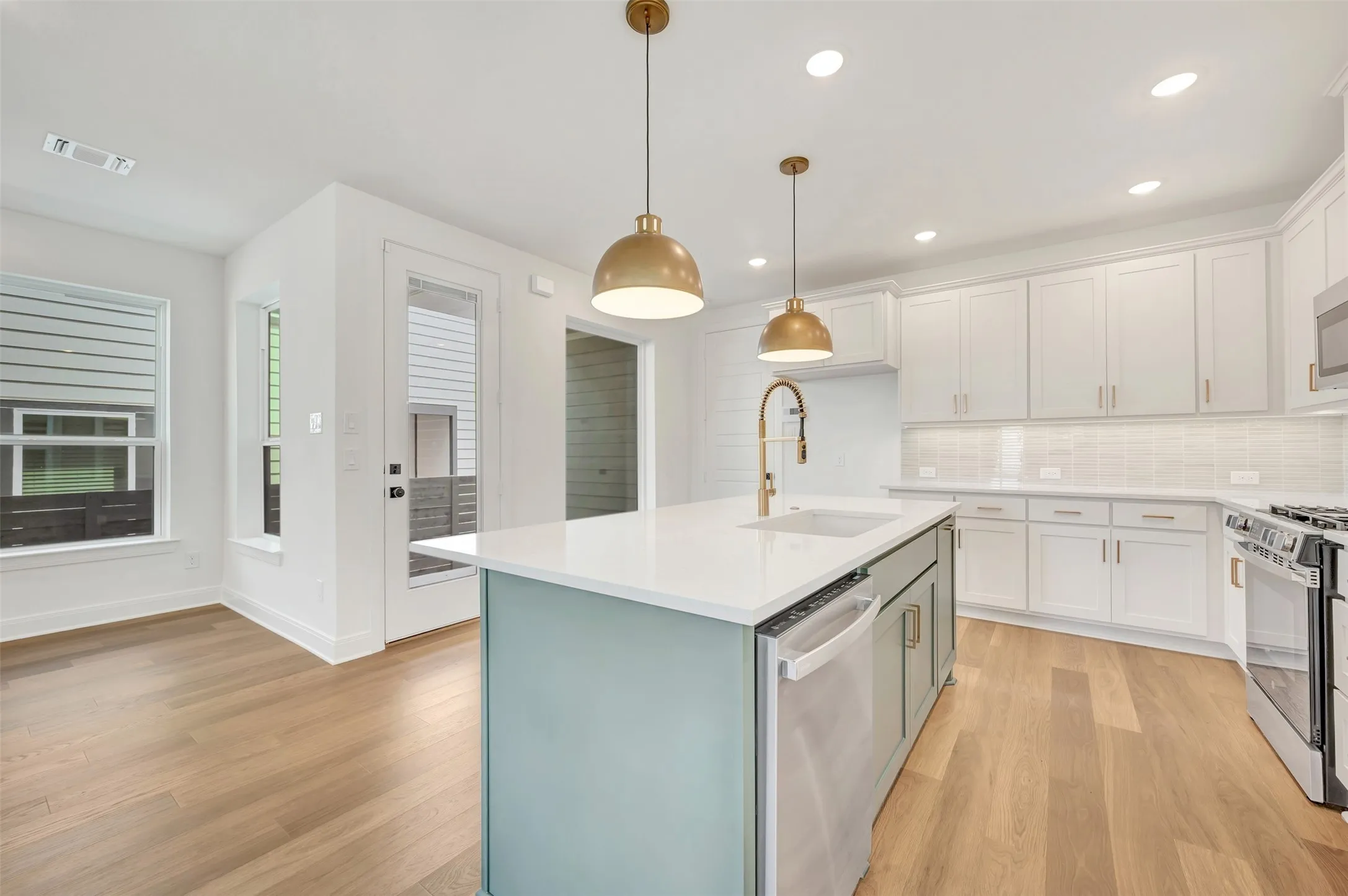 Open-concept kitchen featuring light wood-finish flooring, a central island with a white countertop, two pendant light fixtures, white cabinetry, and stainless steel appliances