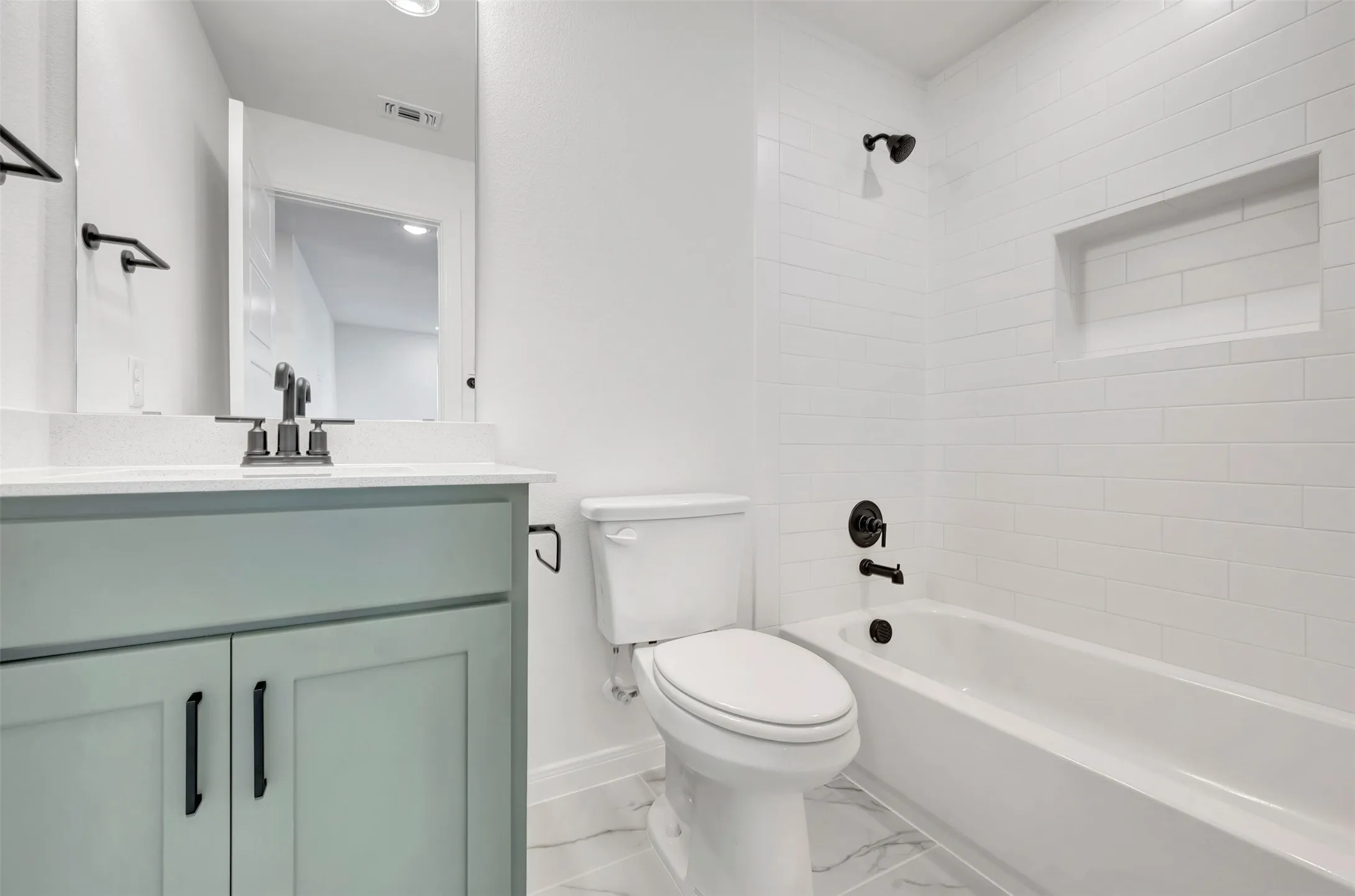 Bathroom featuring a sage green vanity with a white countertop, matte black fixtures, subway tile tub surround with a recessed niche, and marble-look floor tiling