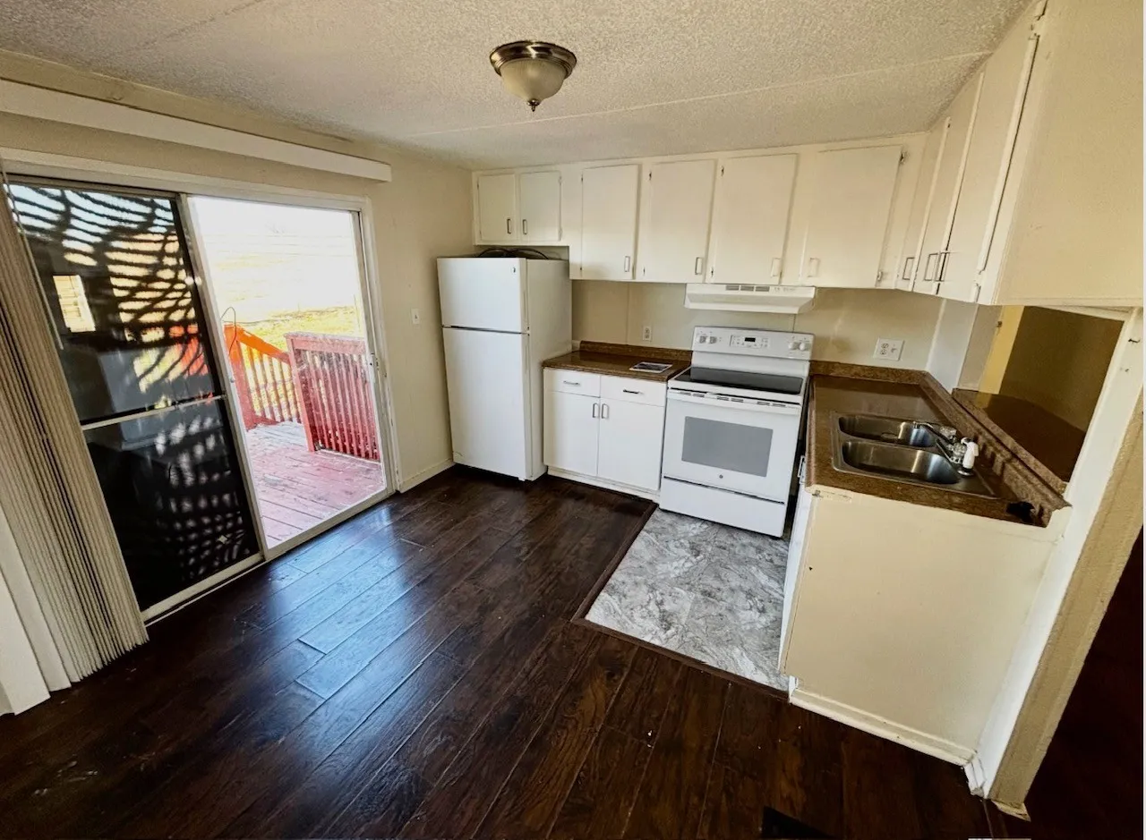 Kitchen featuring white appliances, white cabinetry, a textured ceiling, dark wood-style flooring, and dark countertops