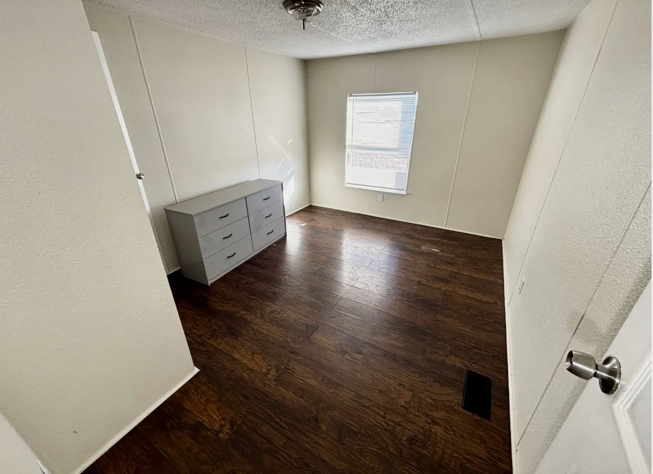 Unfurnished bedroom with a decorative wall, dark wood-style floors, a textured ceiling, and a textured wall