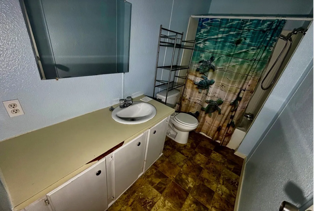 Bathroom with vanity, shower / bath combo with shower curtain, a textured wall, and stone finish floors
