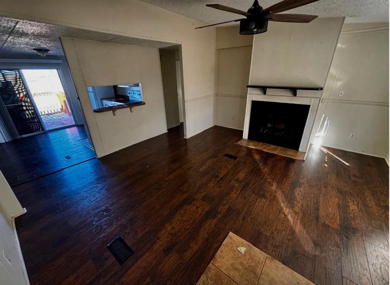 Unfurnished living room with a textured ceiling, a ceiling fan, dark wood-style flooring, and a fireplace with flush hearth