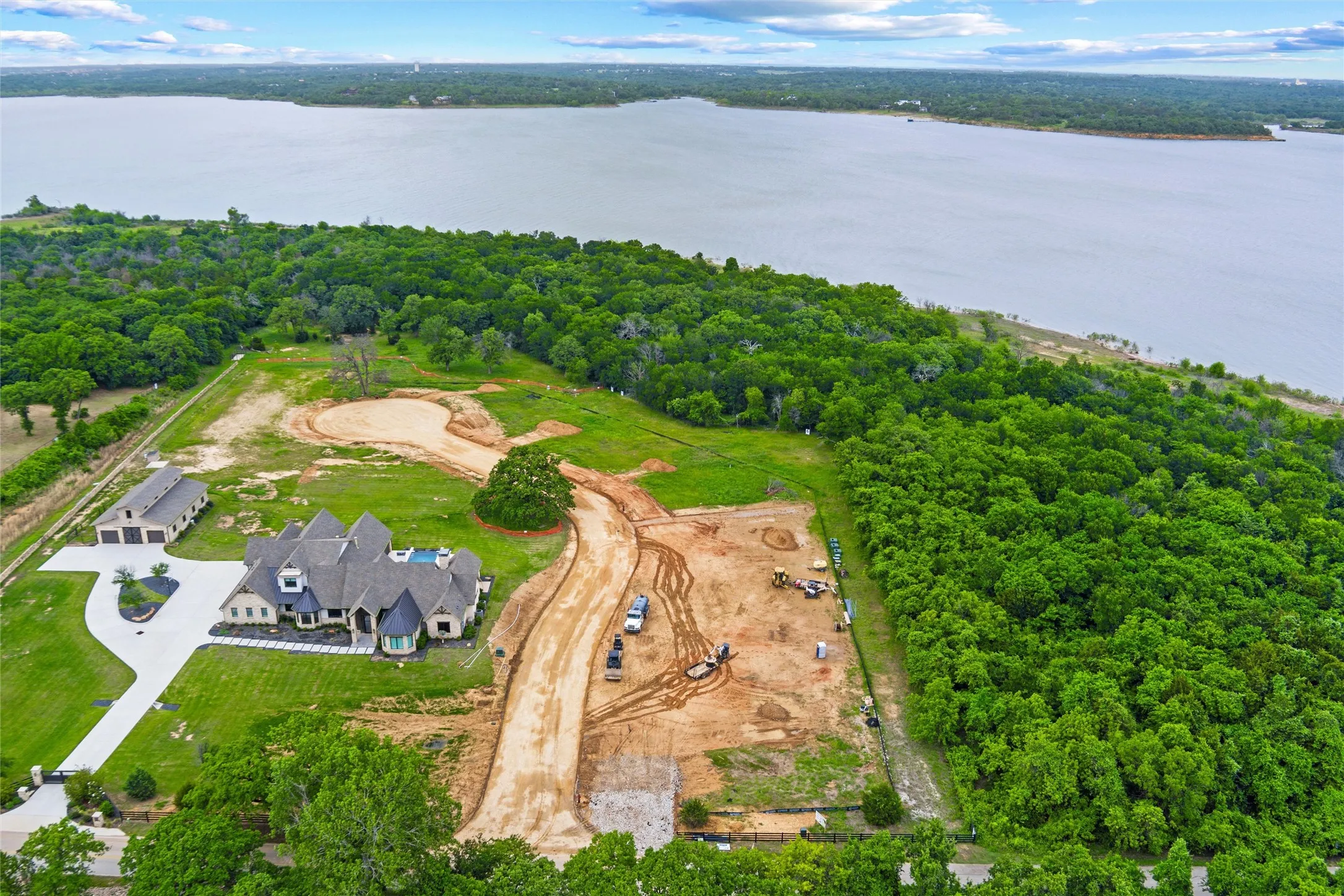 Expansive property featuring a large body of water, extensive wooded areas, a custom residence with a multi-gabled roof, a detached auxiliary building, and a paved circular driveway