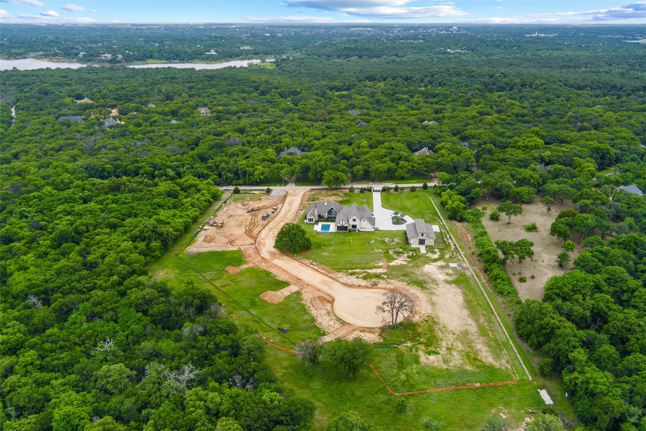 Aerial perspective showcasing extensive tree coverage, a developed residential property with a swimming pool, and multiple building sites in various stages of development