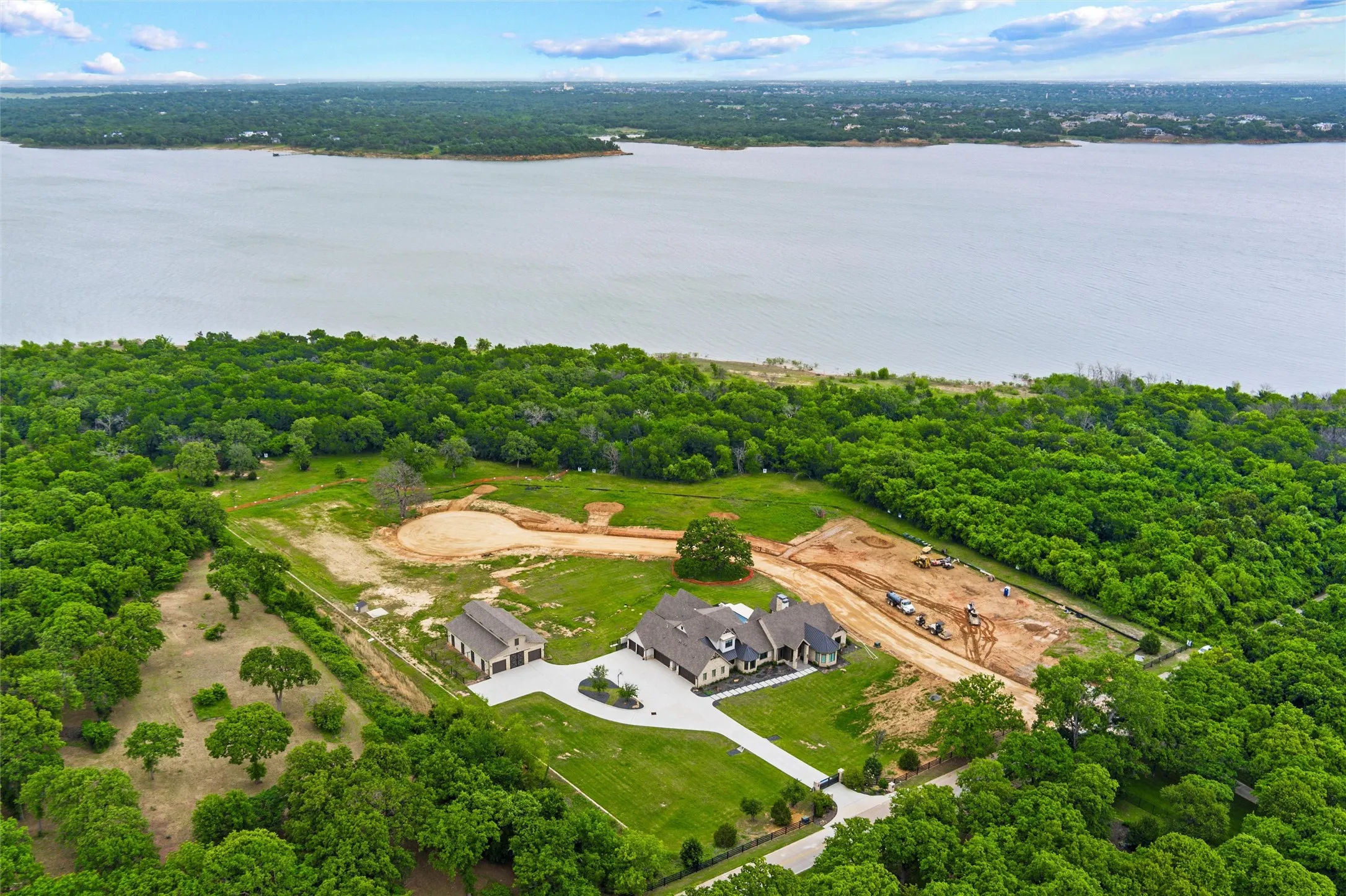 Expansive waterfront property featuring a large residence, detached garage, extensive green space, and mature tree coverage