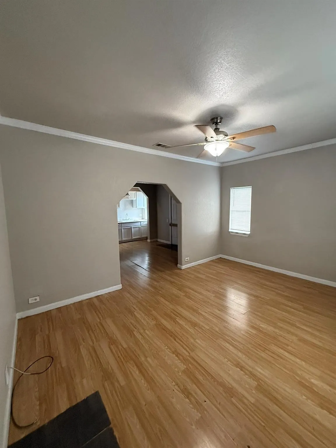 Unfurnished room featuring light wood-style flooring, ceiling fan, ornamental molding, arched walkways, and plenty of natural light