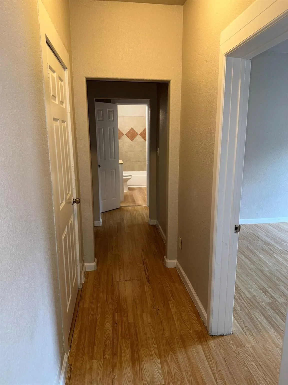 Corridor with light wood-style flooring and a textured wall